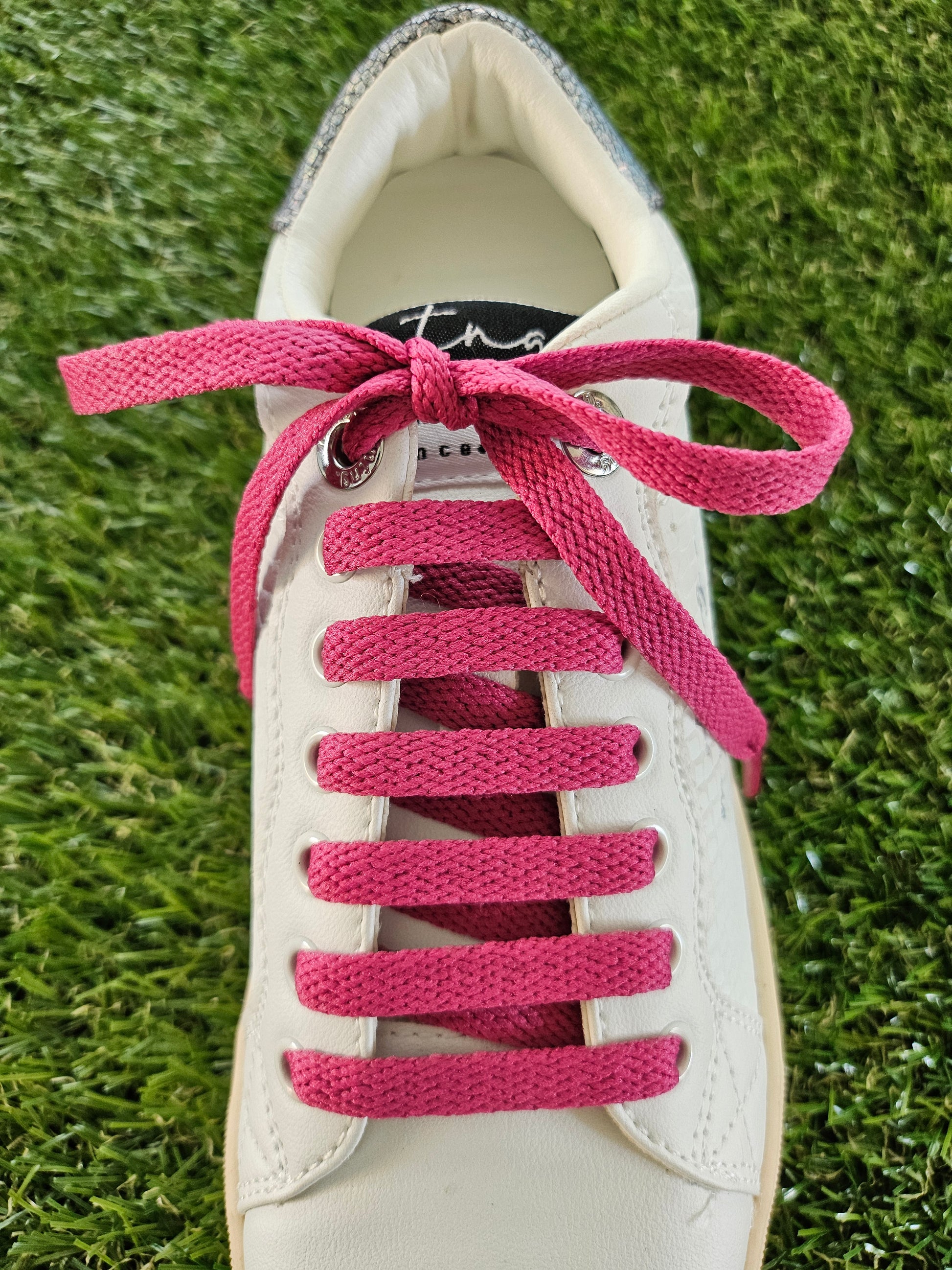 raspberry pink shoelaces in a white trainer on green grass