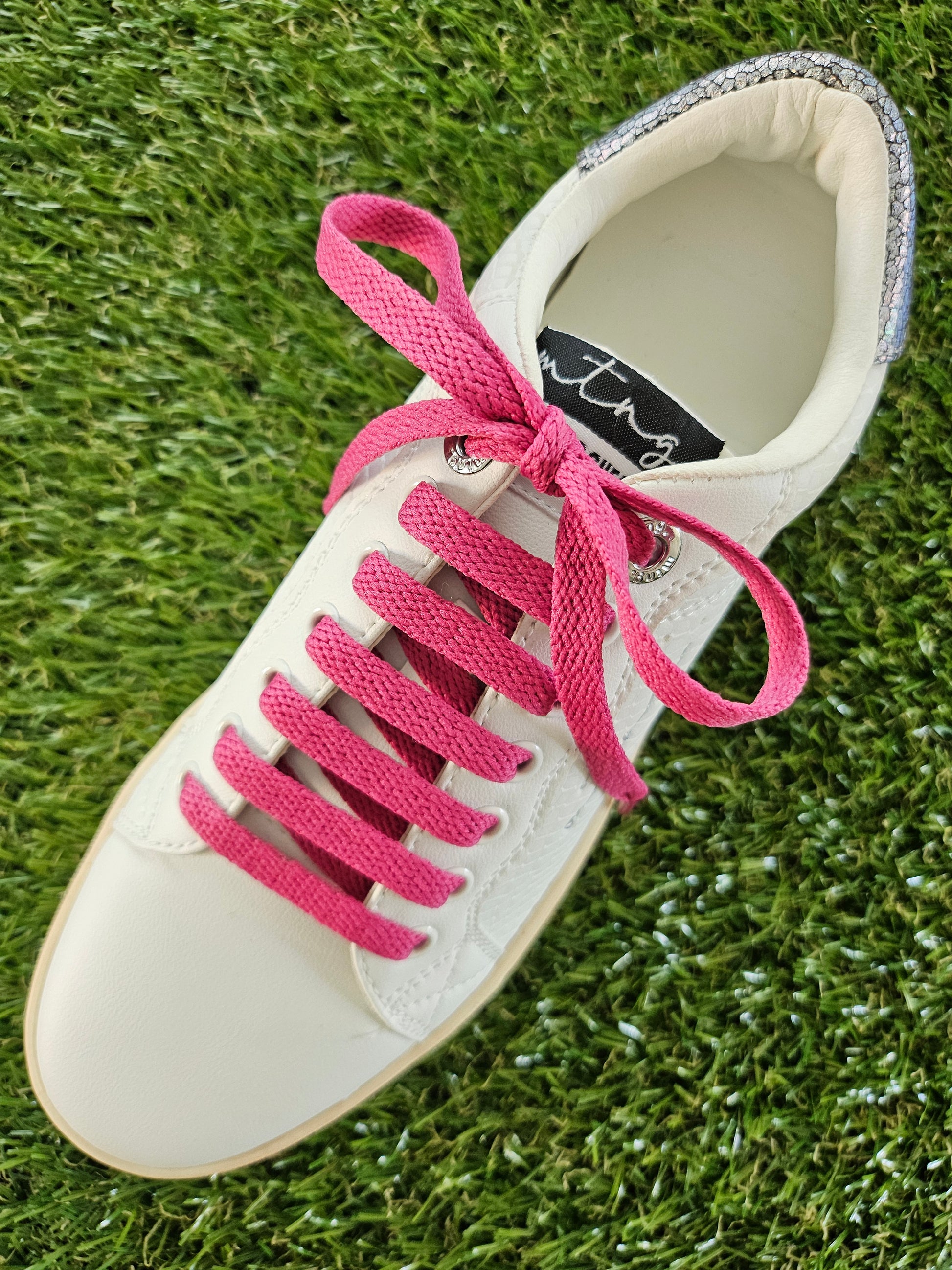raspberry pink shoelaces in a white trainer on green grass