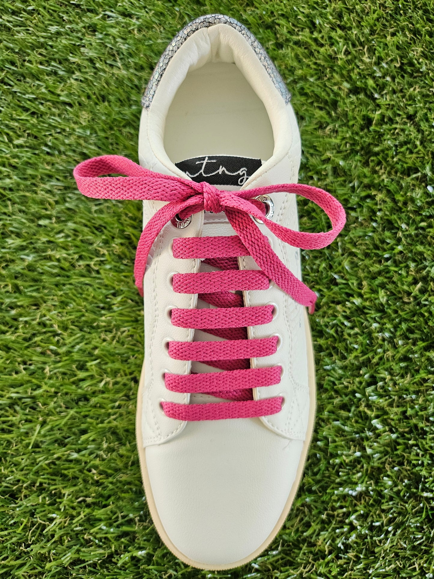 raspberry pink shoelaces in a white trainer on green grass