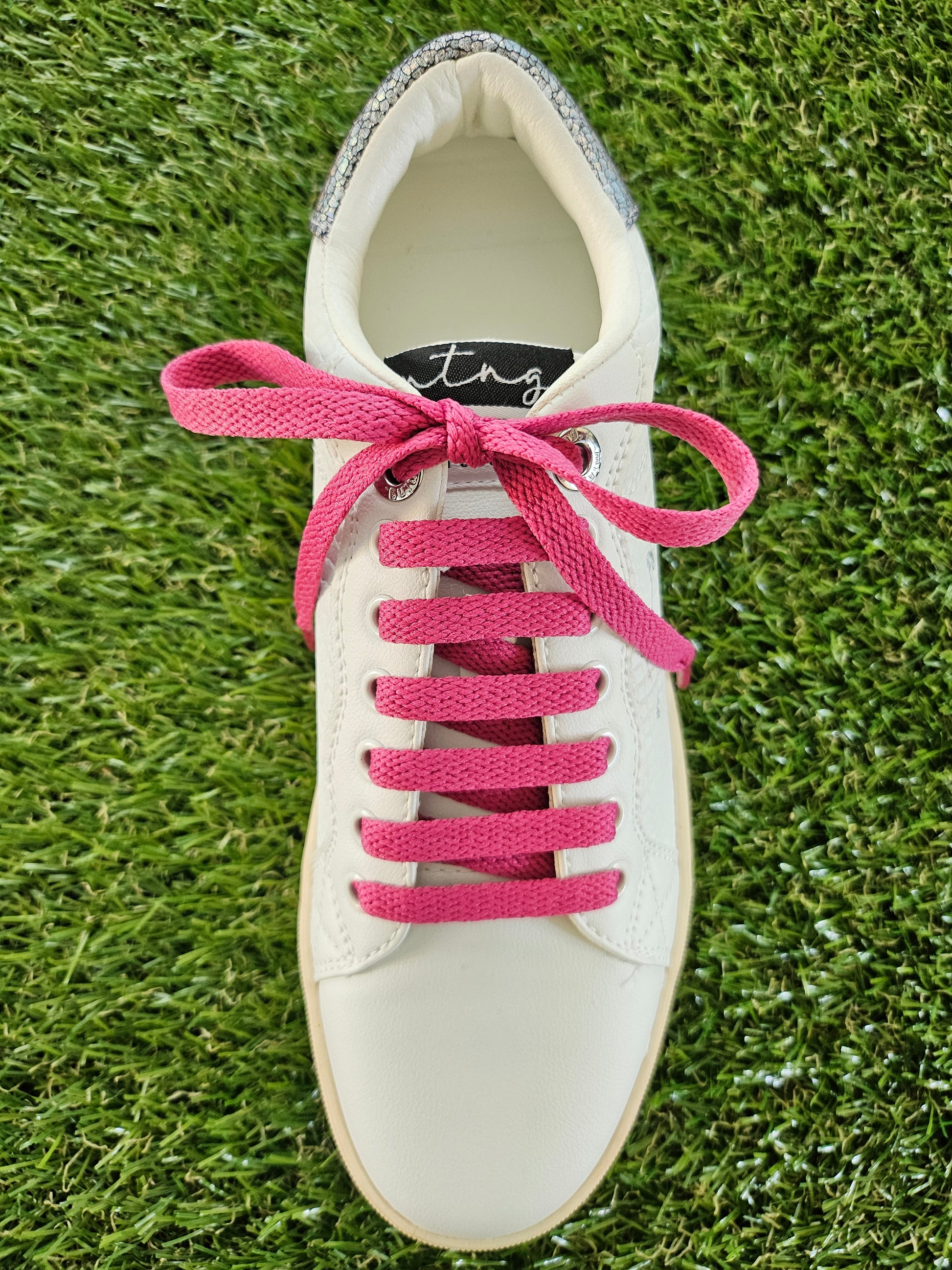 raspberry pink shoelaces in a white trainer on green grass
