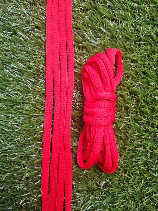 Red classic oval shoelaces on green grass