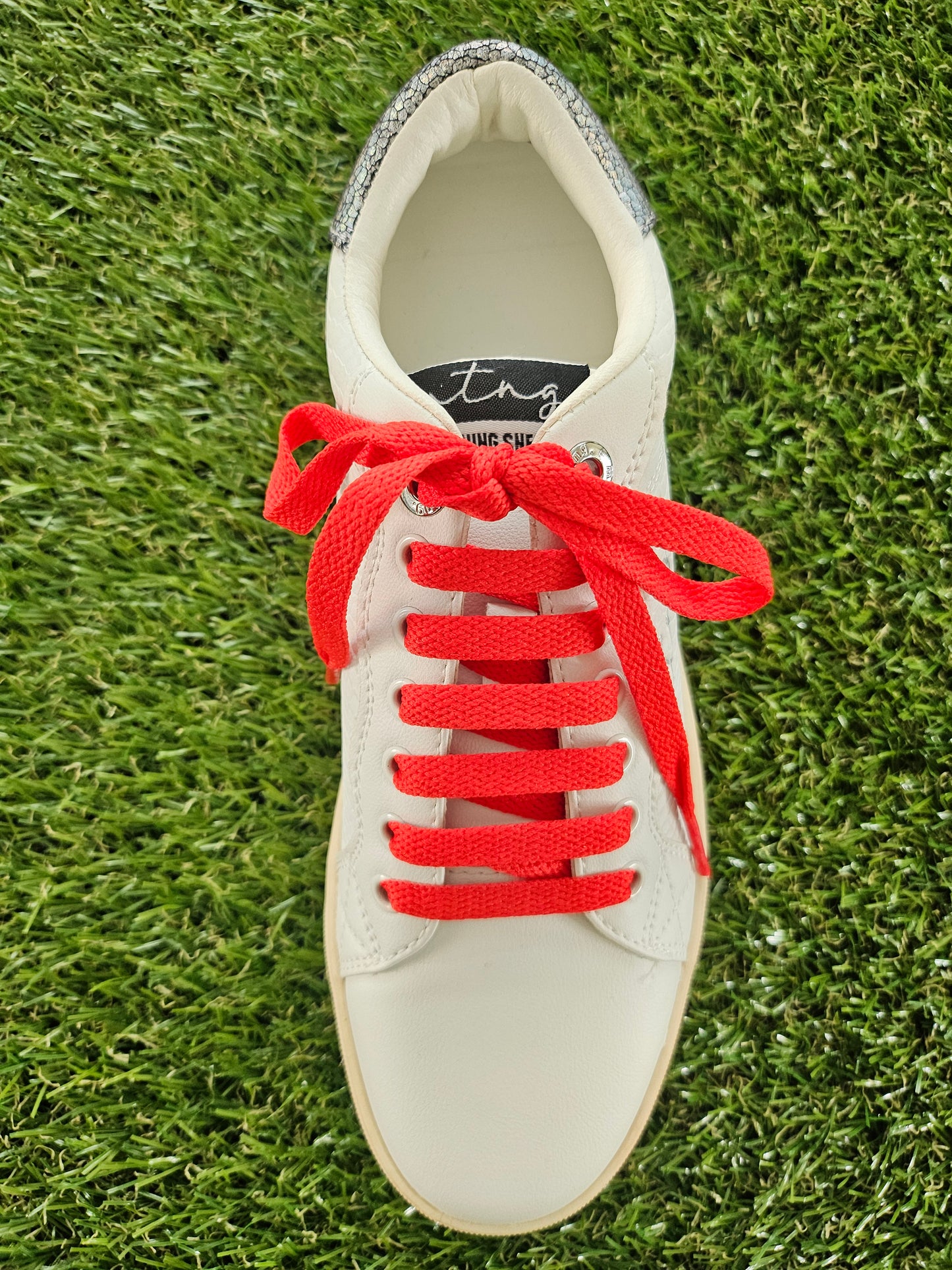 White sneaker with red laces on a grass background