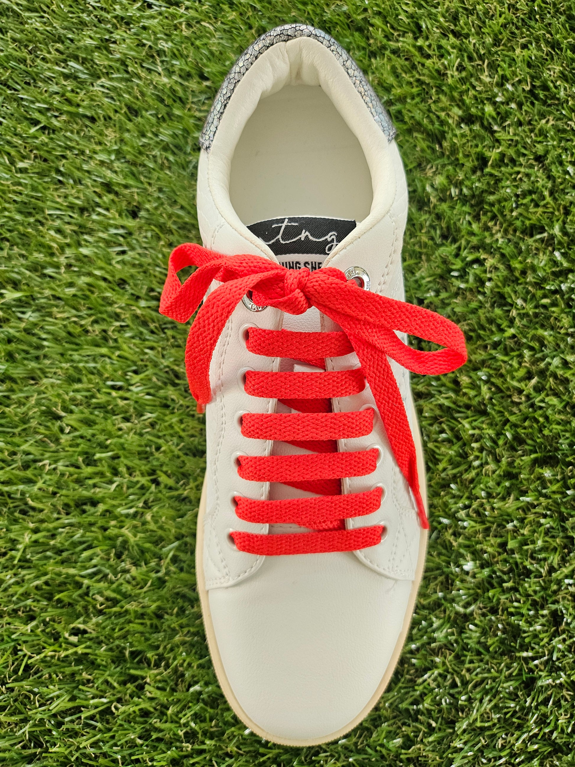 White sneaker with red laces on a grass background
