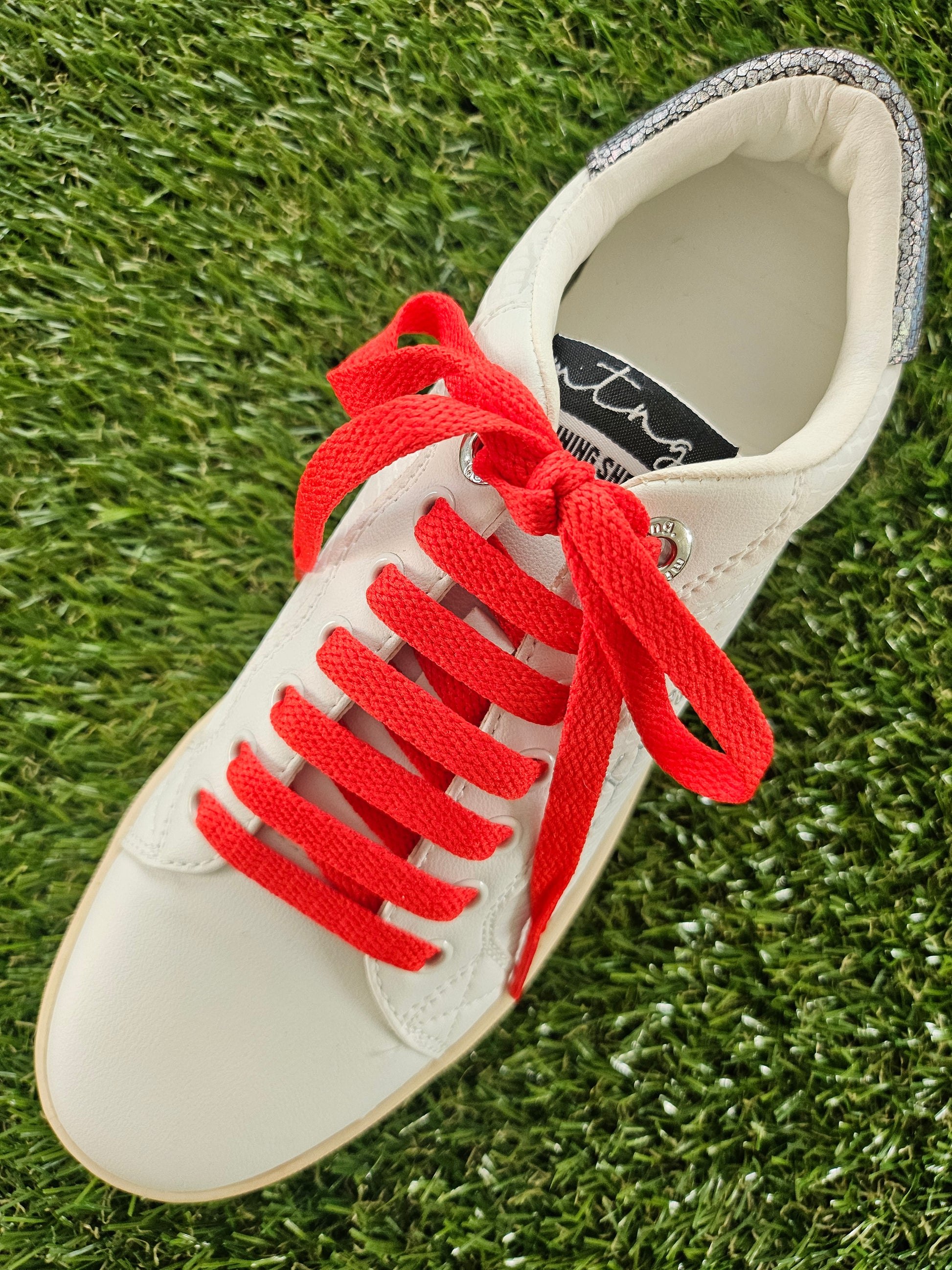 White sneaker with red laces on a grass background