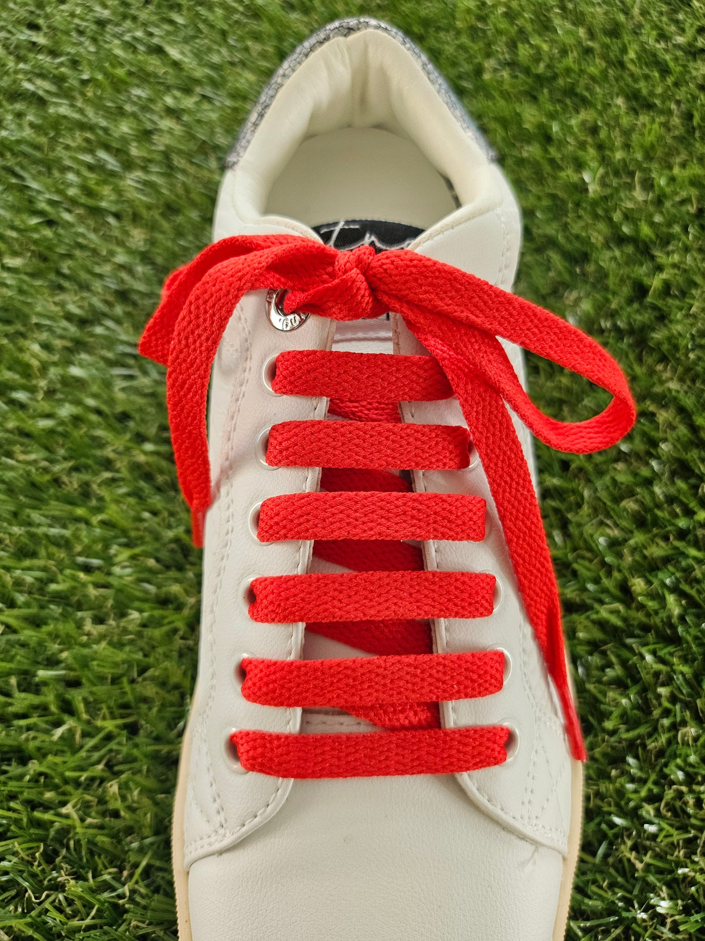 White sneaker with red laces on a grass background