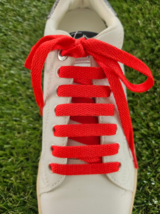 White sneaker with red laces on a grass background