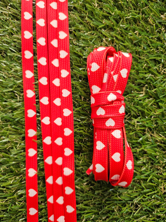 Red shoelace with white heart patterns on a grass background