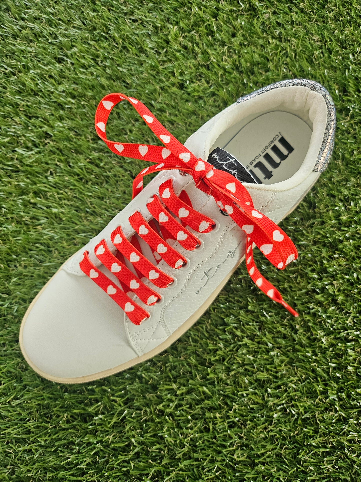 White sneaker with red and white love heart shoelaces on grass