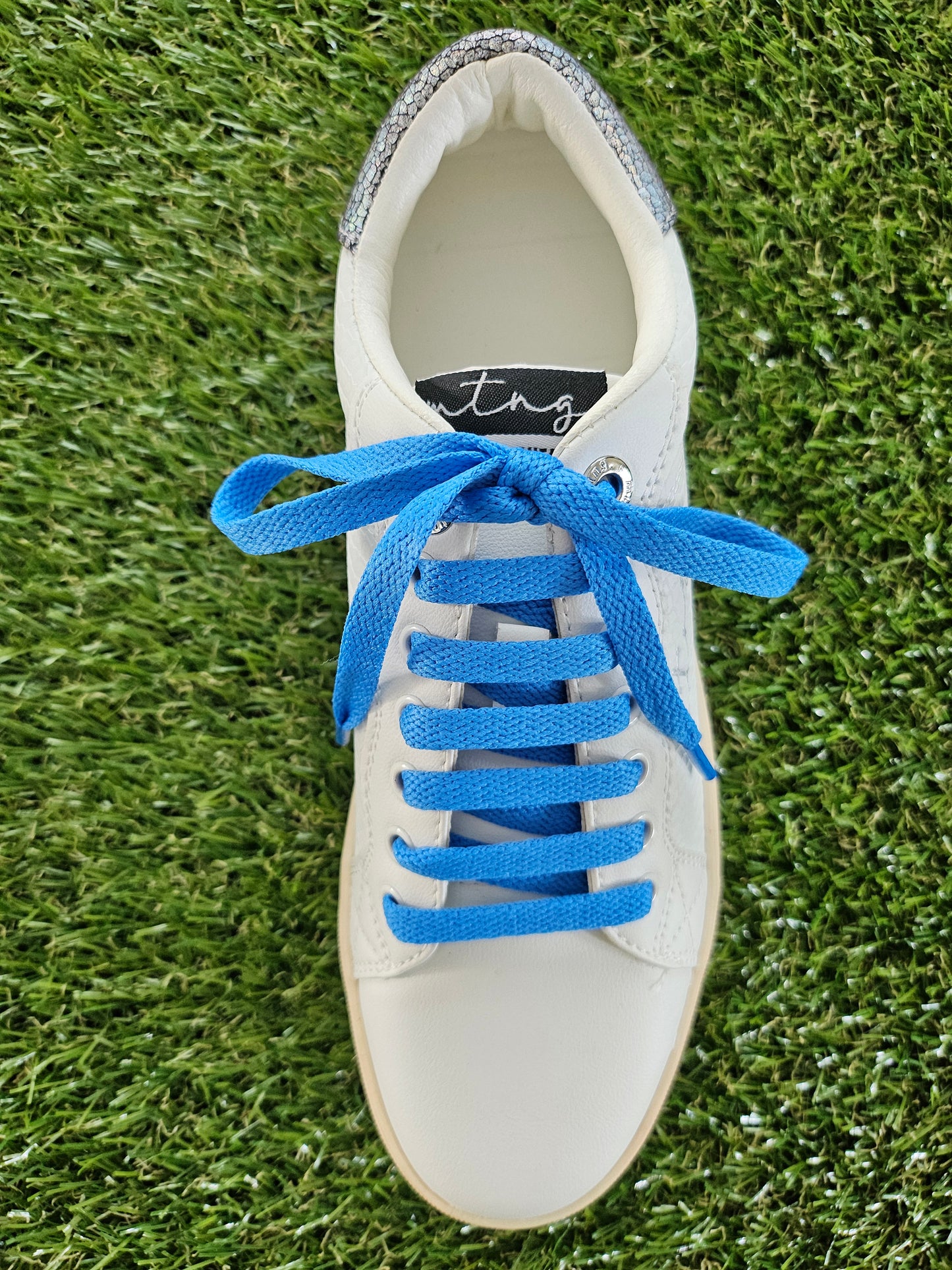 White sneaker with blue laces on a grass background