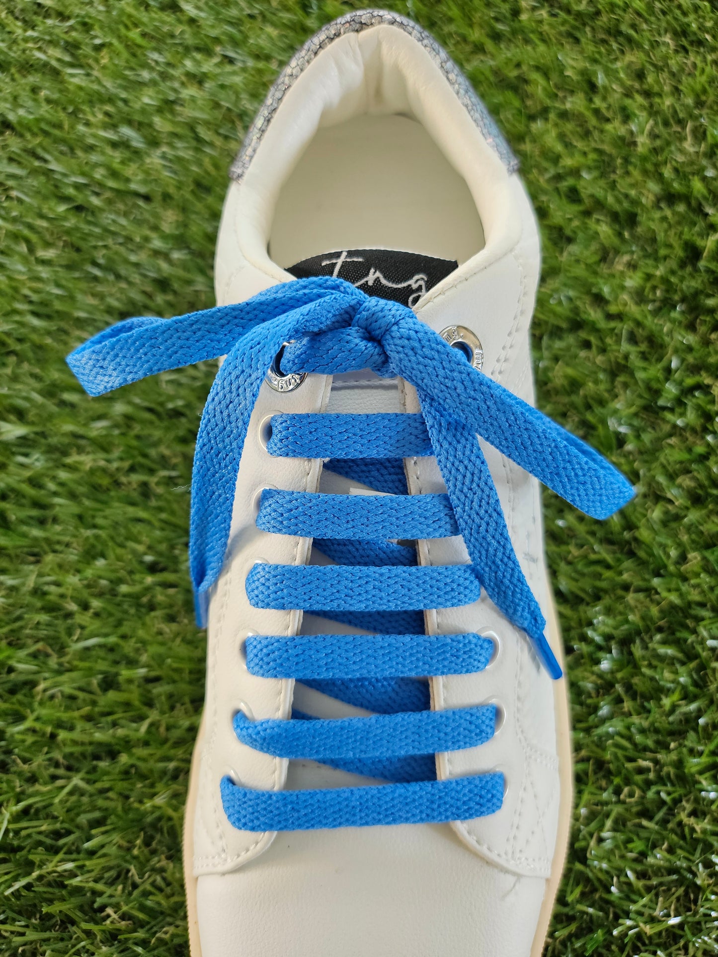 White sneaker with blue shoelaces on a grass background