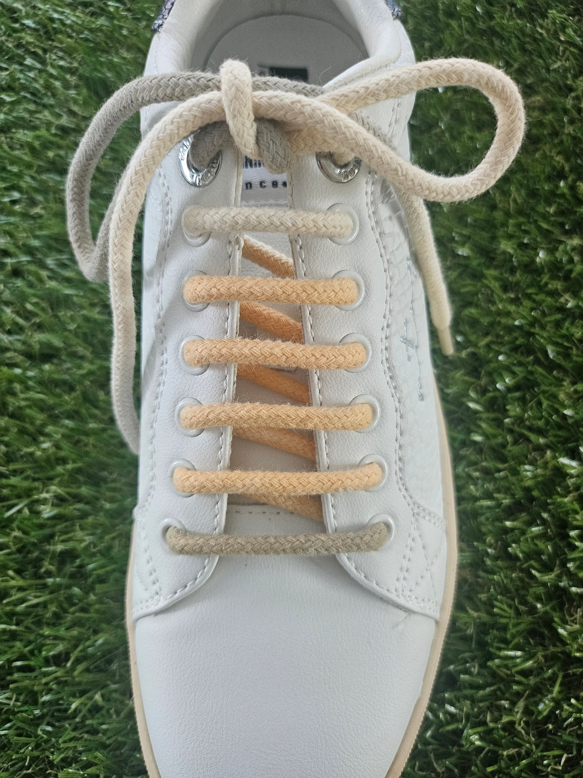 White sneaker with beige laces on a grass background