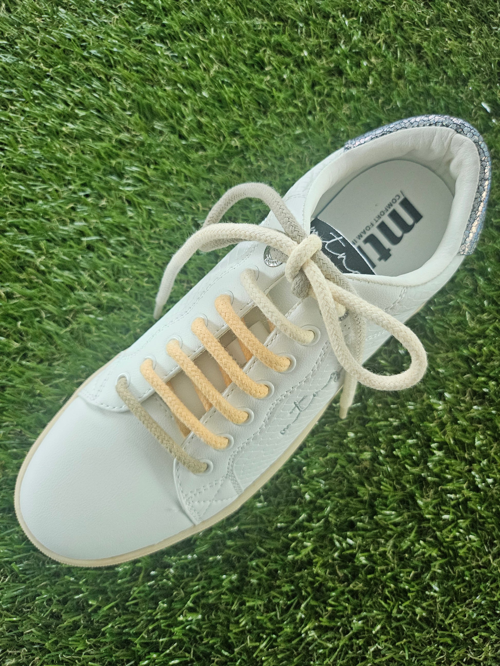 White sneaker with beige laces on grass