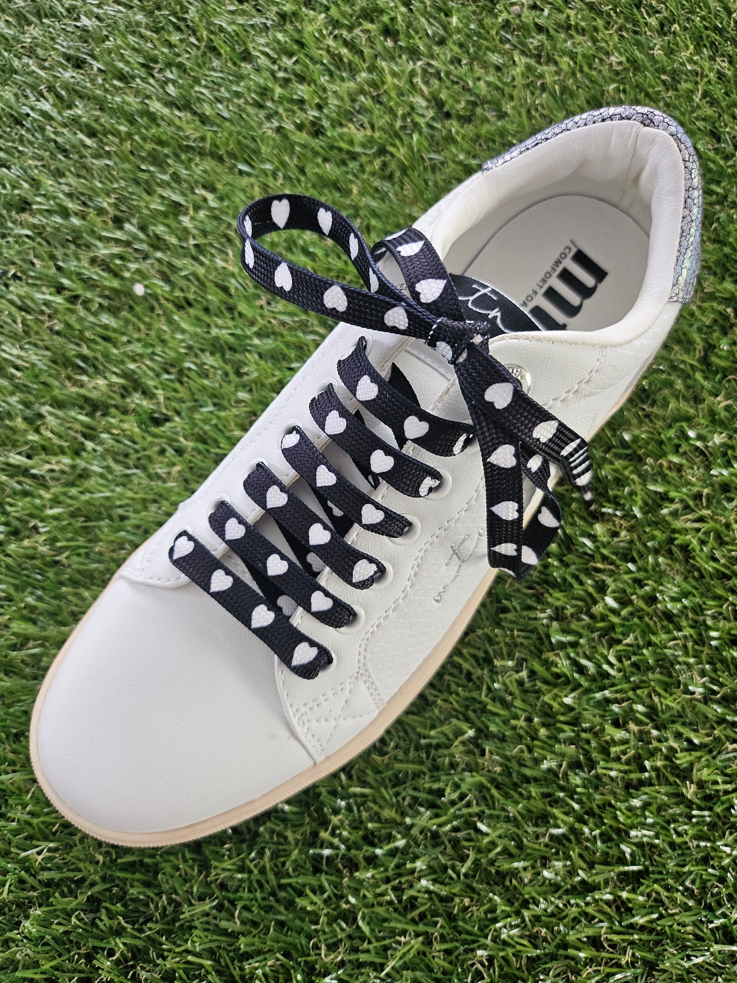 White sneaker with black and white heart laces on a grass background