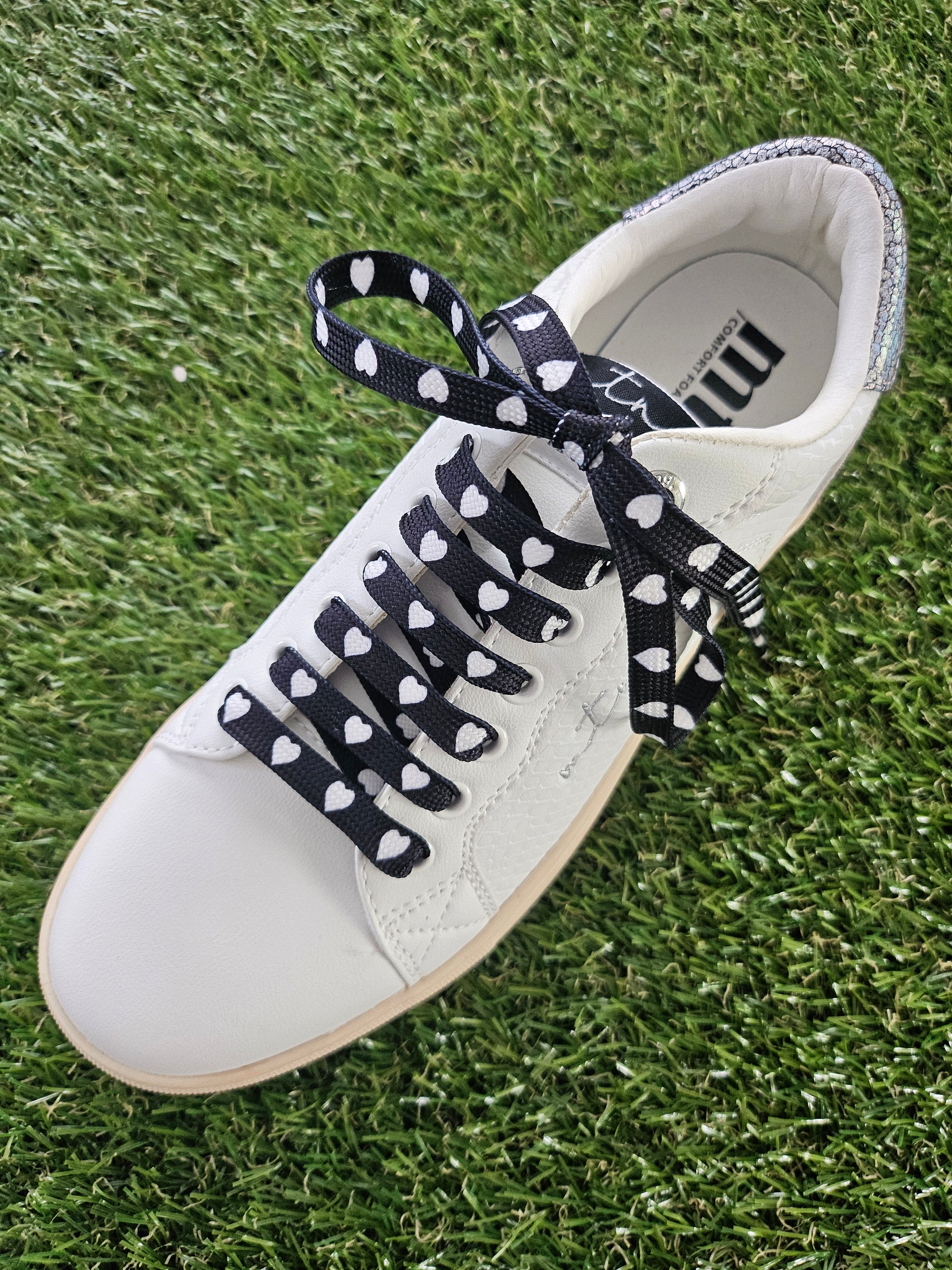 White sneaker with black and white heart laces on a grass background