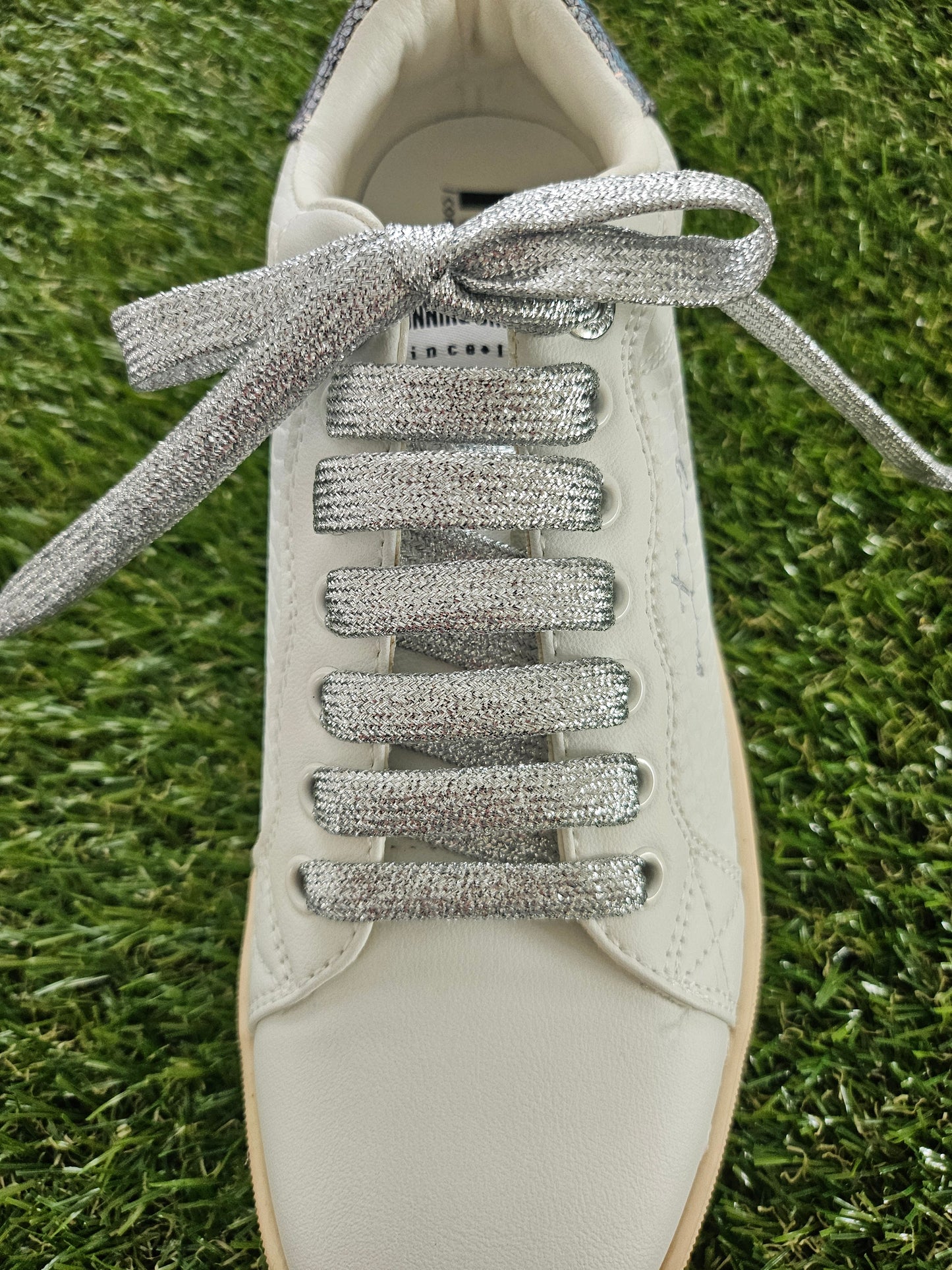 White sneaker with silver glittery laces on a grass background