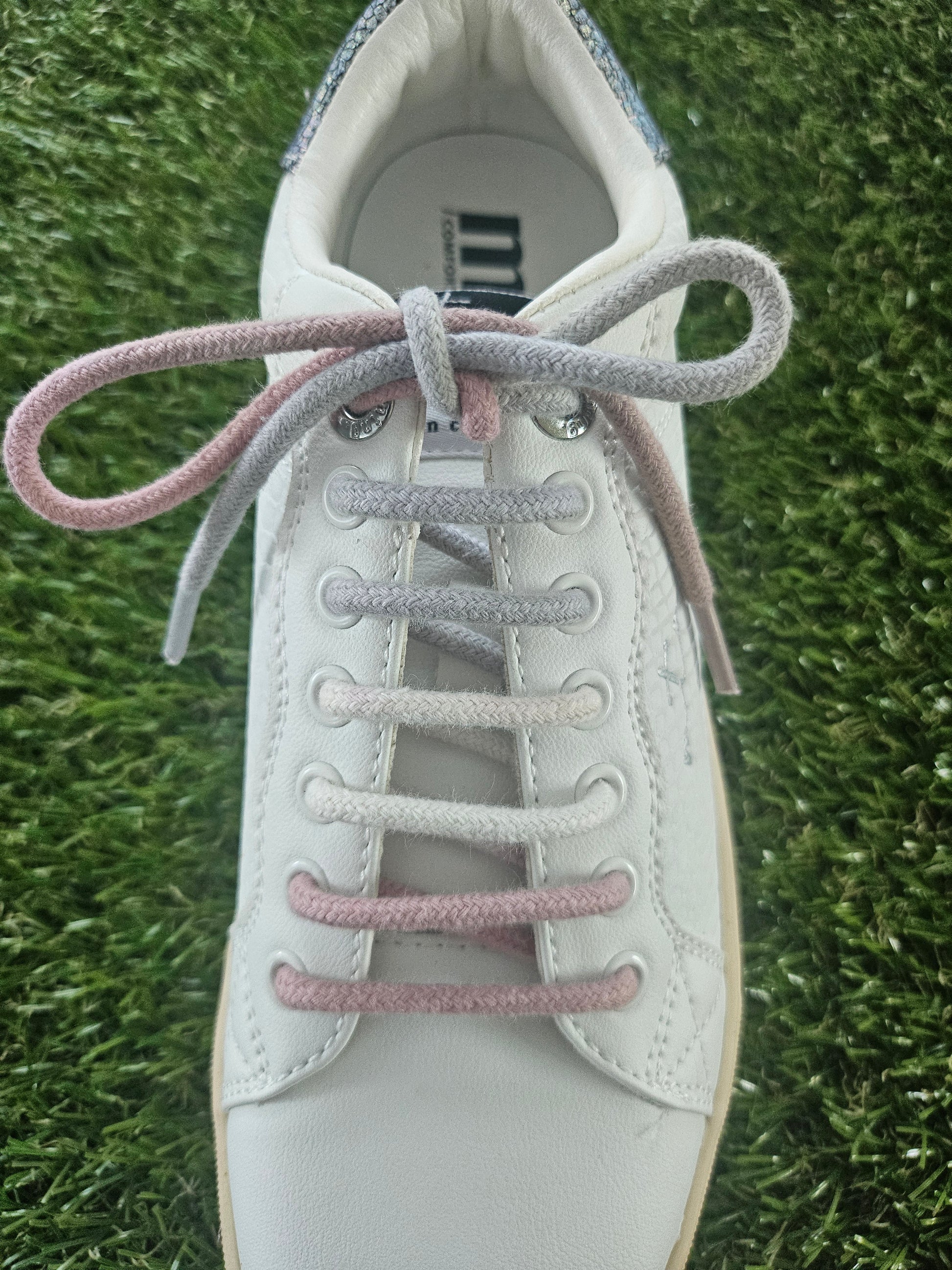 White sneaker with pink laces on a grass background