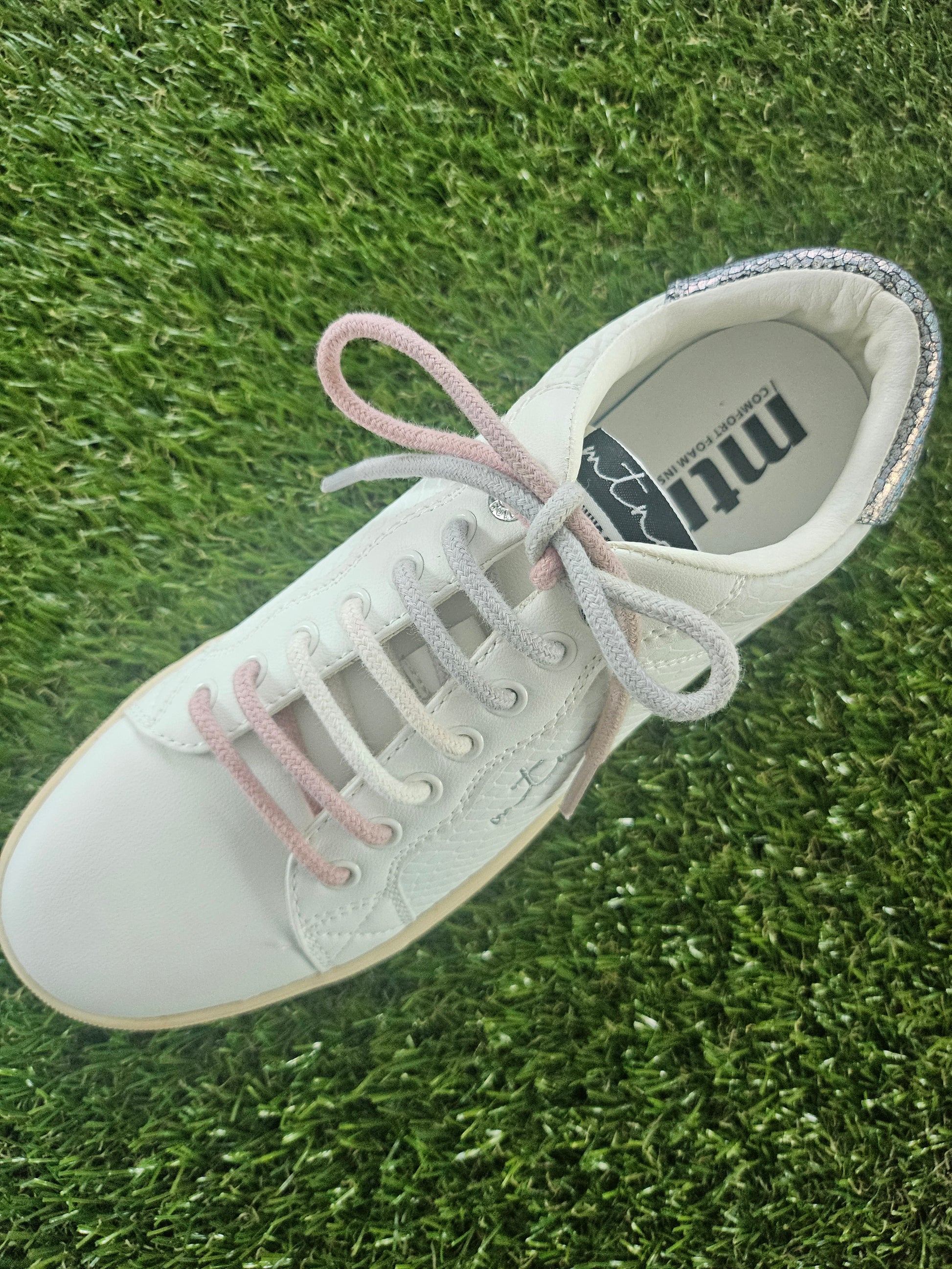 White sneaker with pink laces on grass