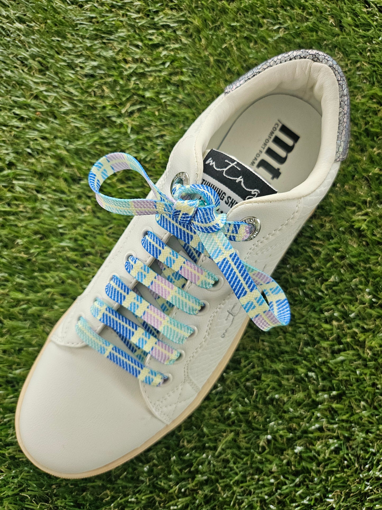 White sneaker with colourful scottish tartan laces on a grass background