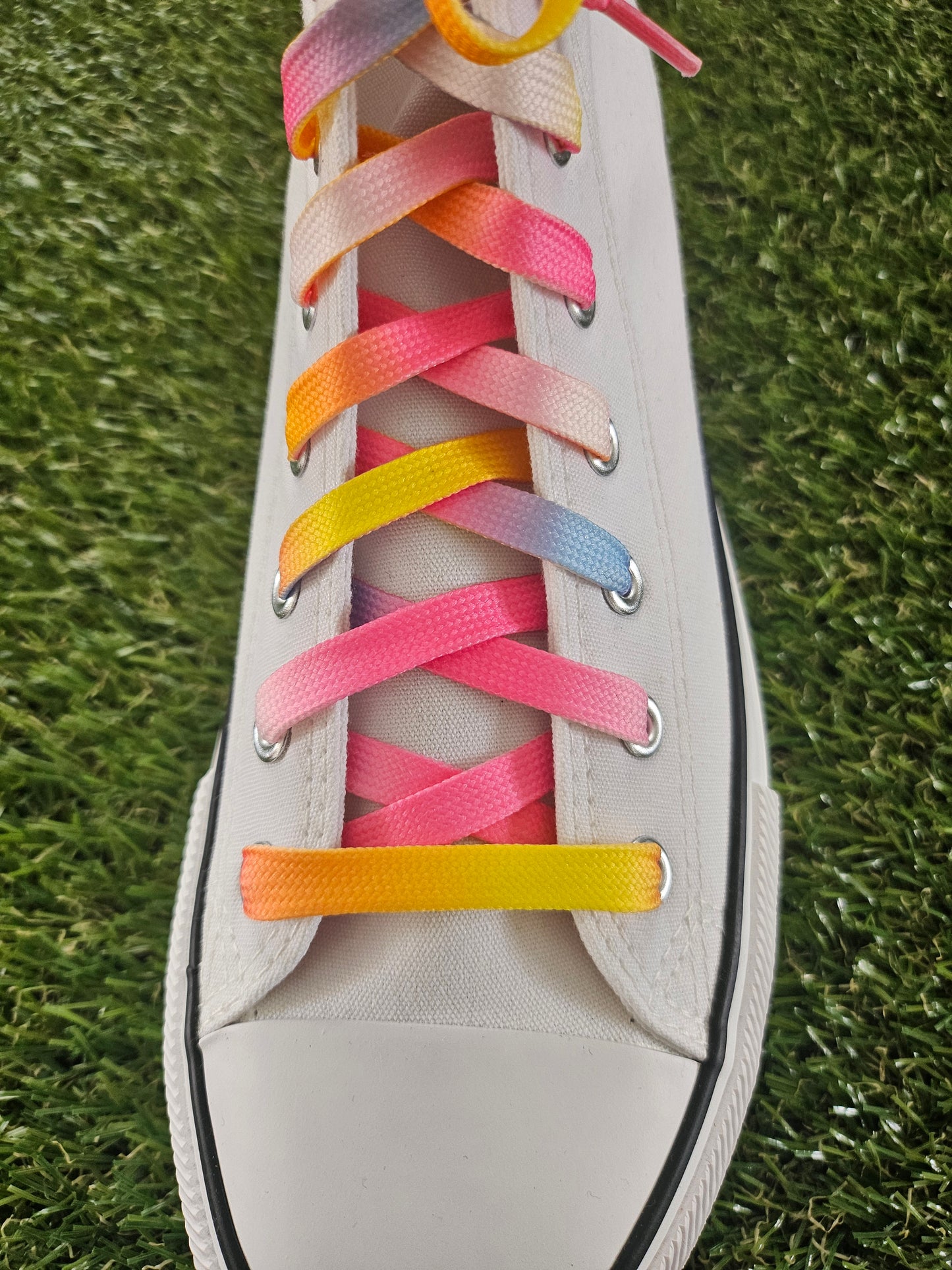 White sneaker with colourful laces on a grass background