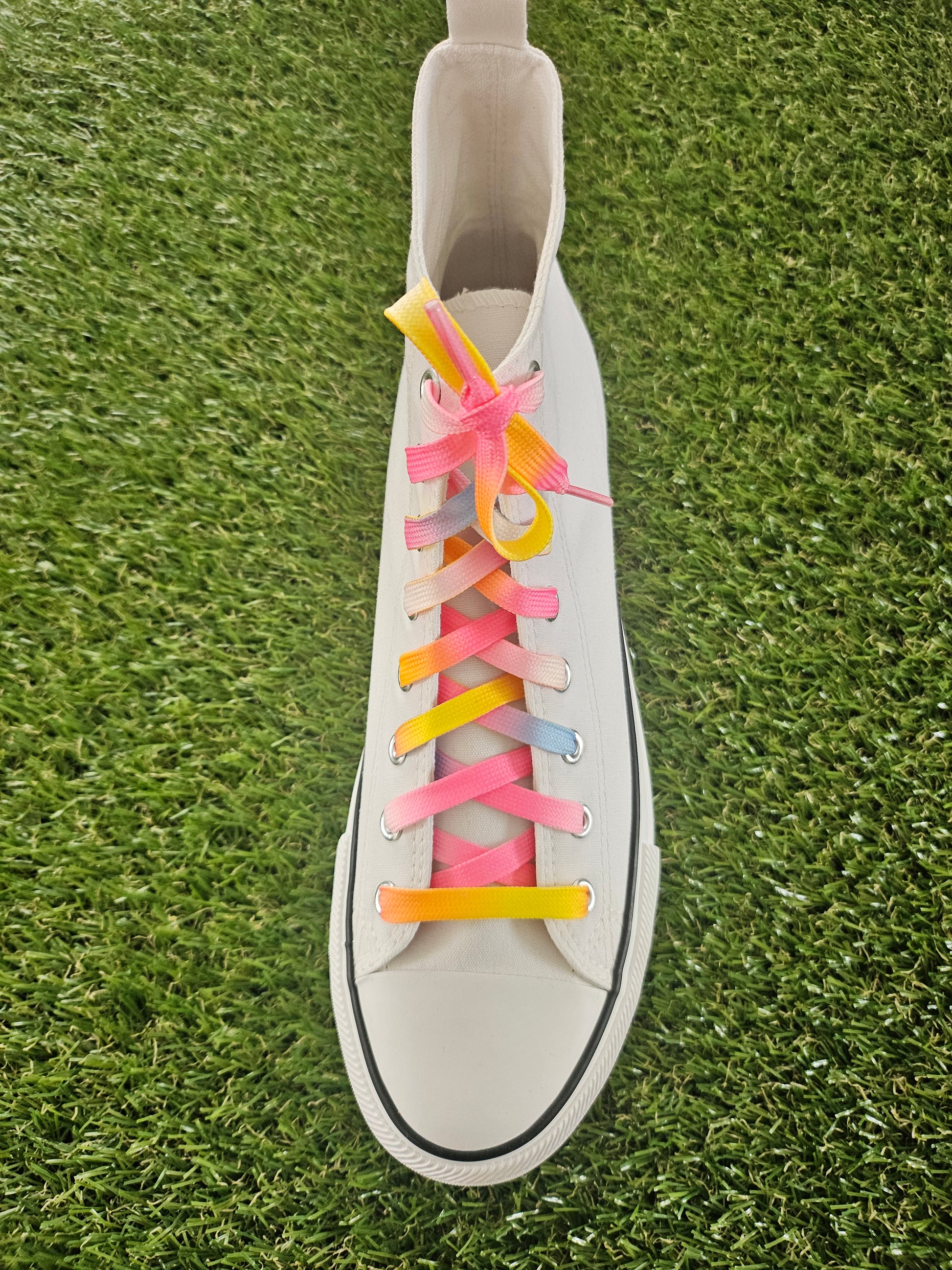 White high top trainer with colourful pastel shoelaces on a grass background
