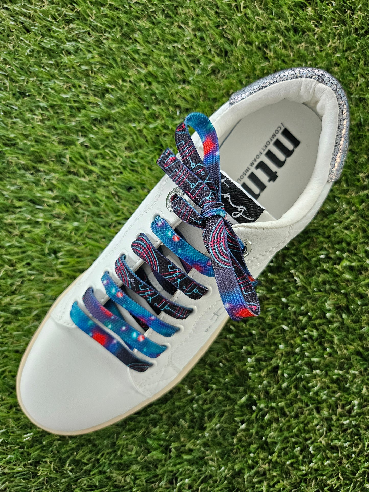 White trainer with space patterned colorful laces on a grass background