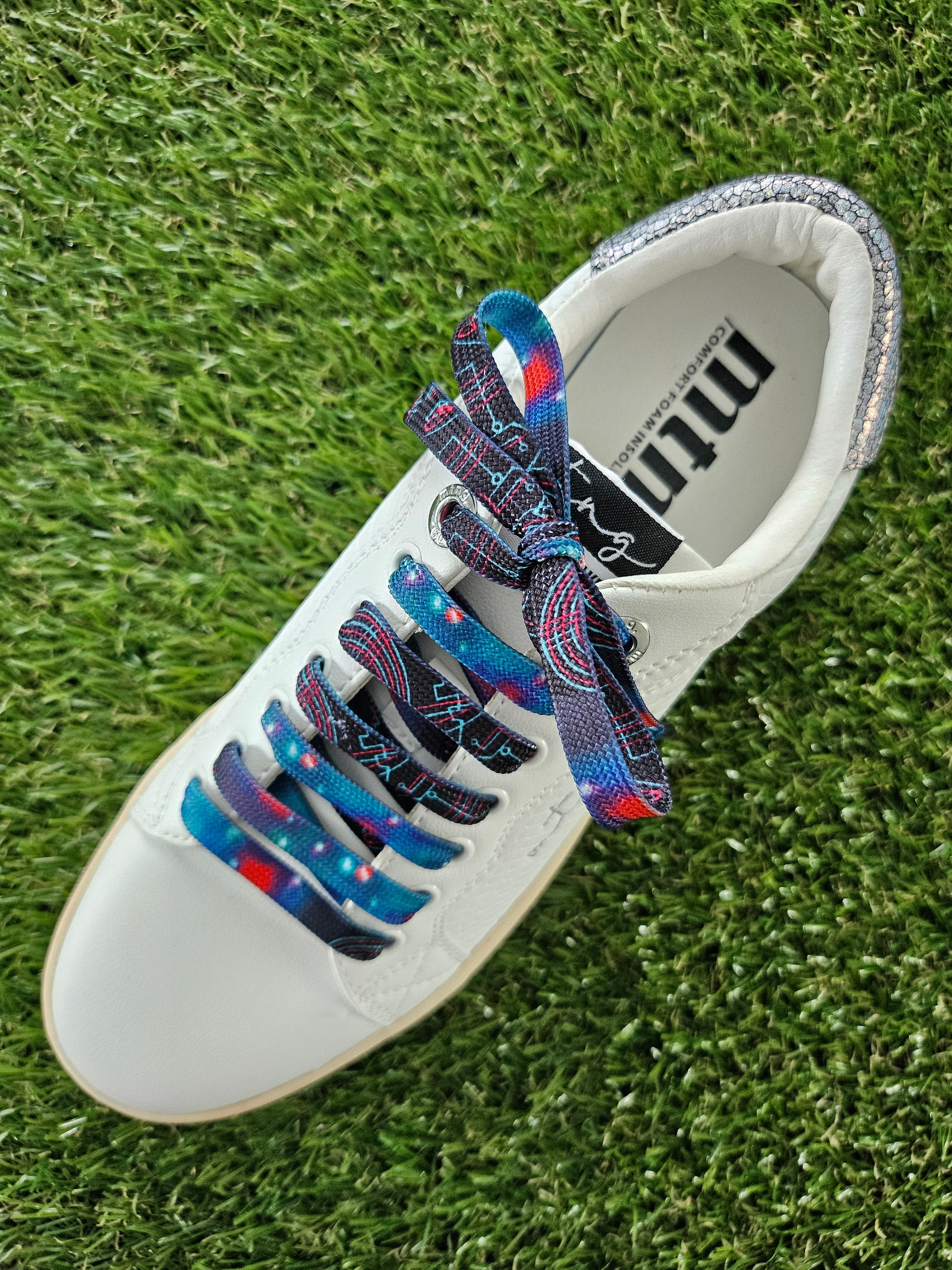 White trainer with space patterned colorful laces on a grass background