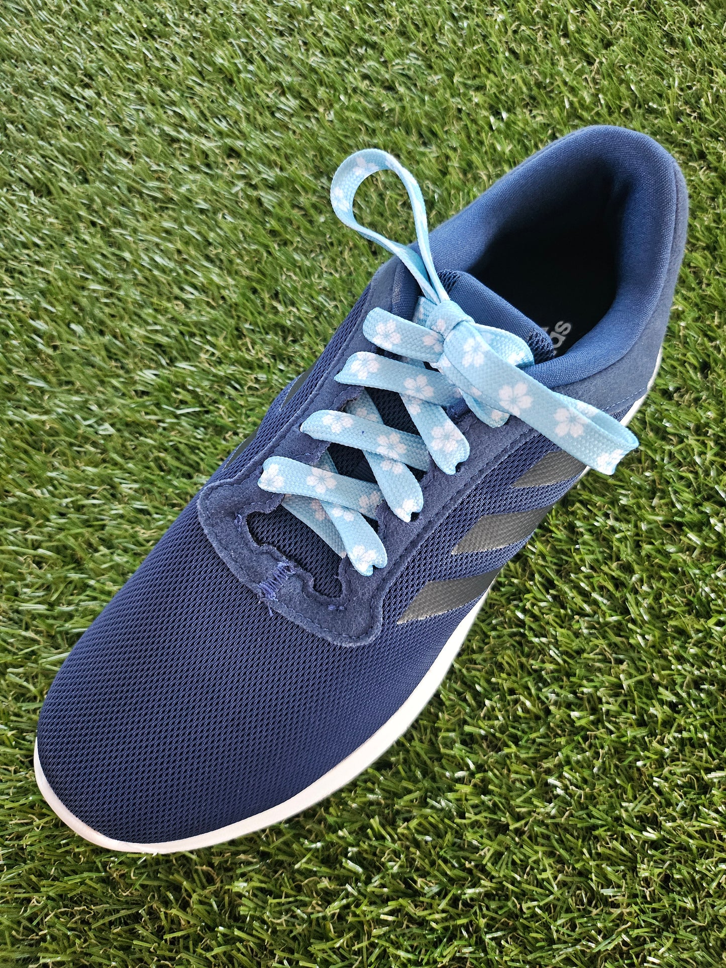 Blue athletic shoe with light blue laces on grass