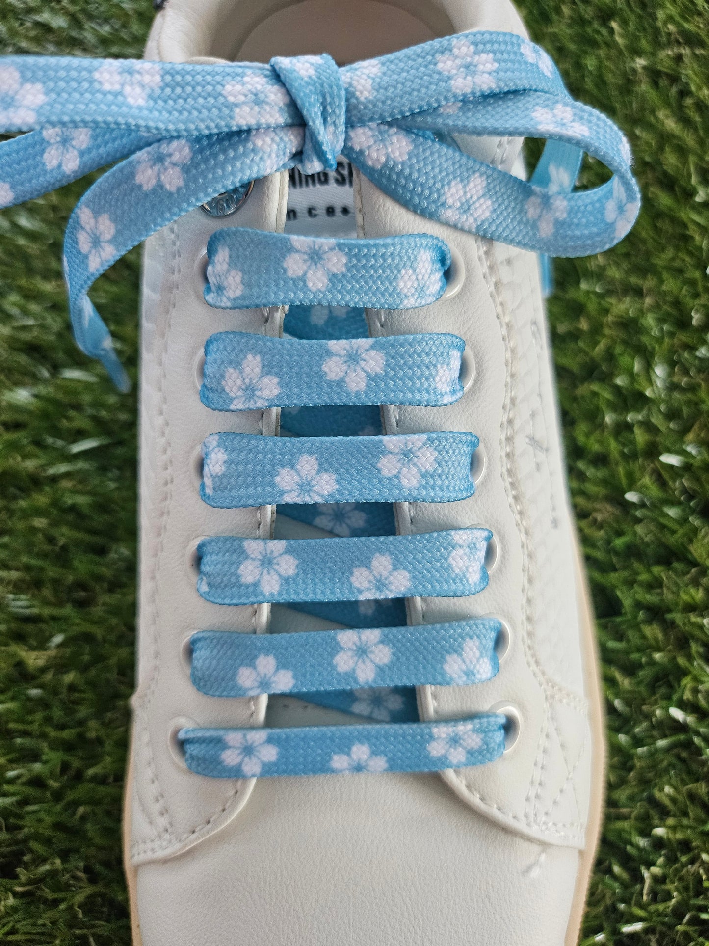 White trainer with blue floral lace on grass background