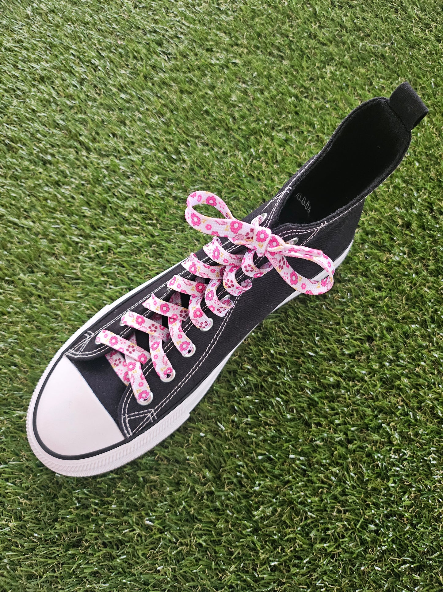 black converse boot with pink flowers on a white shoelace on grass