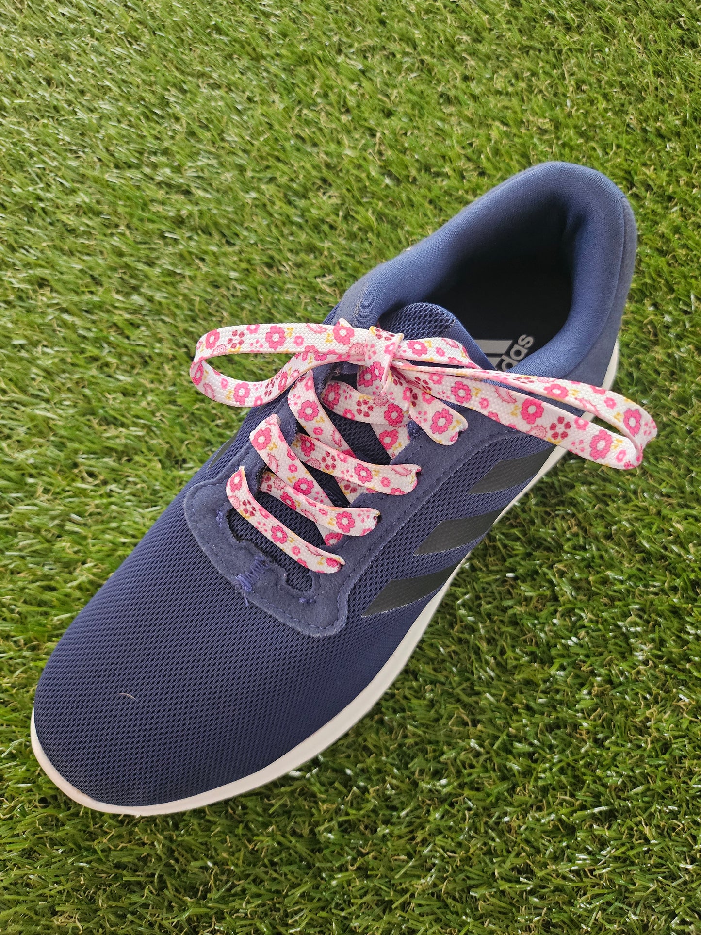 Navy blue shoe with pink floral laces on grass