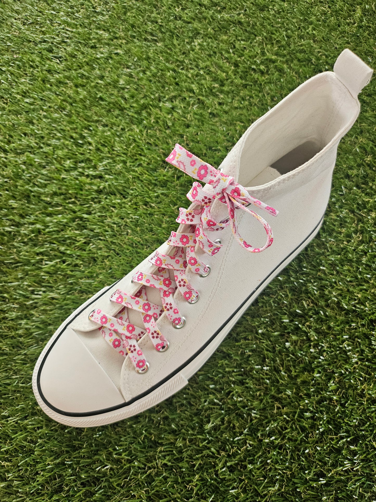 white converse boot with pink flowers on a white shoelace on grass