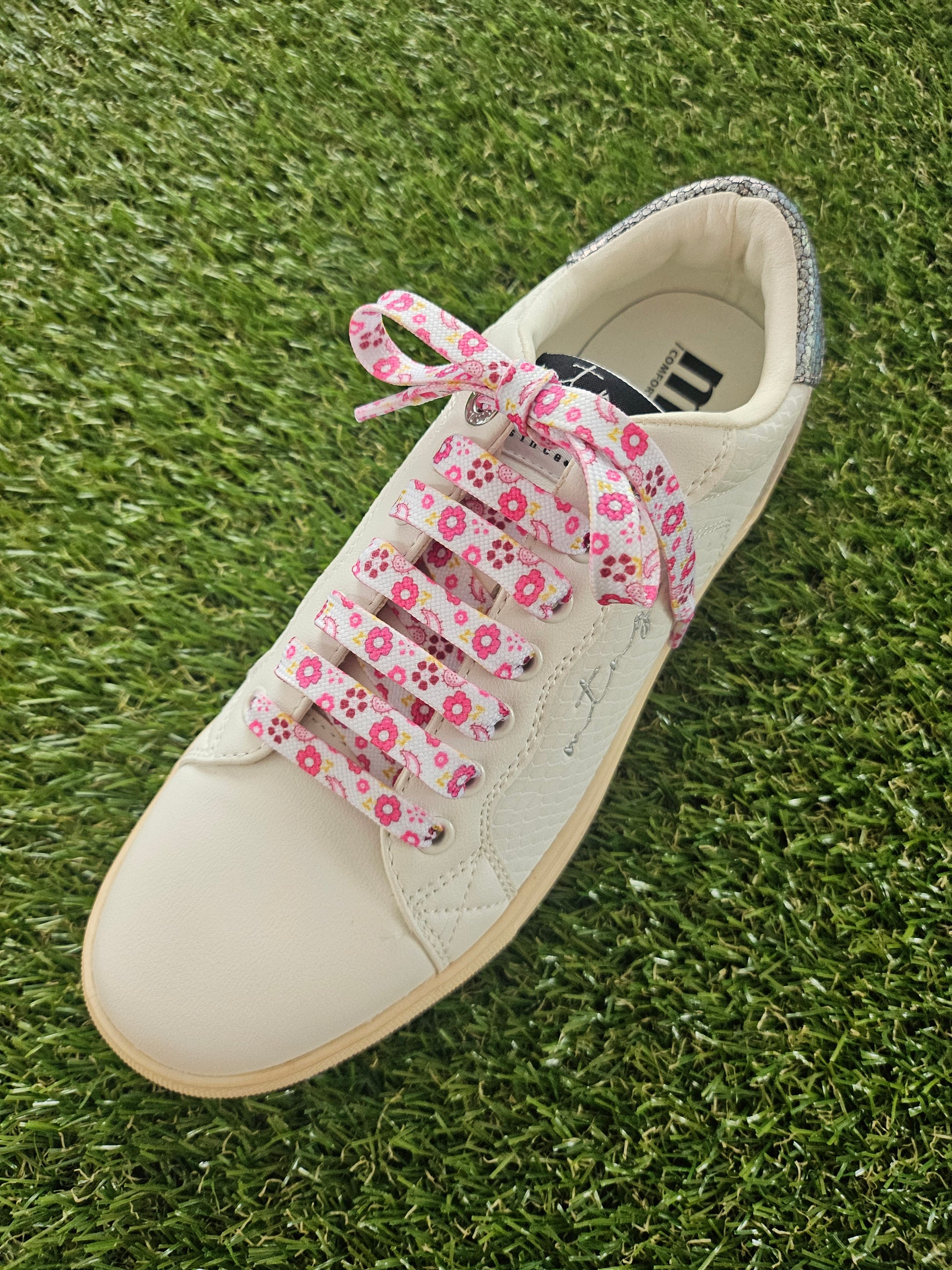 White sneaker with pink floral laces on a grass background