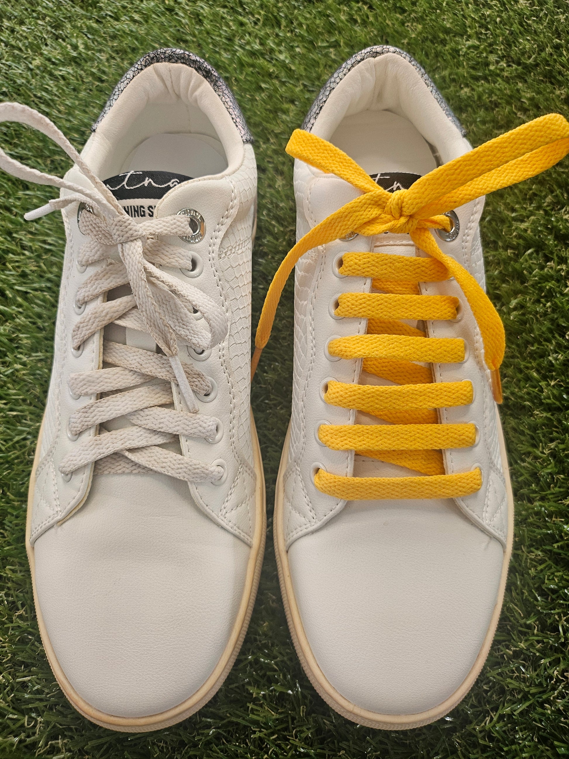 White sneakers with yellow laces on grass