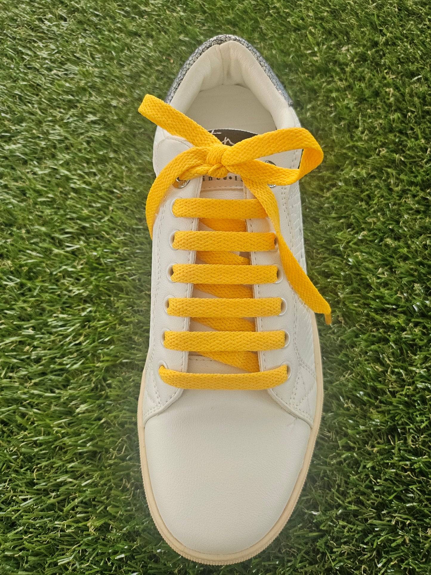White sneaker with yellow laces on a grass background