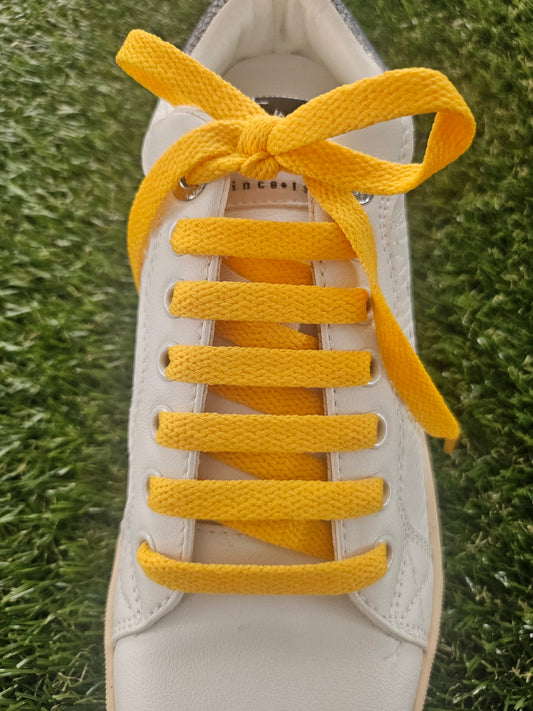 White sneaker with yellow shoelaces on a grass background