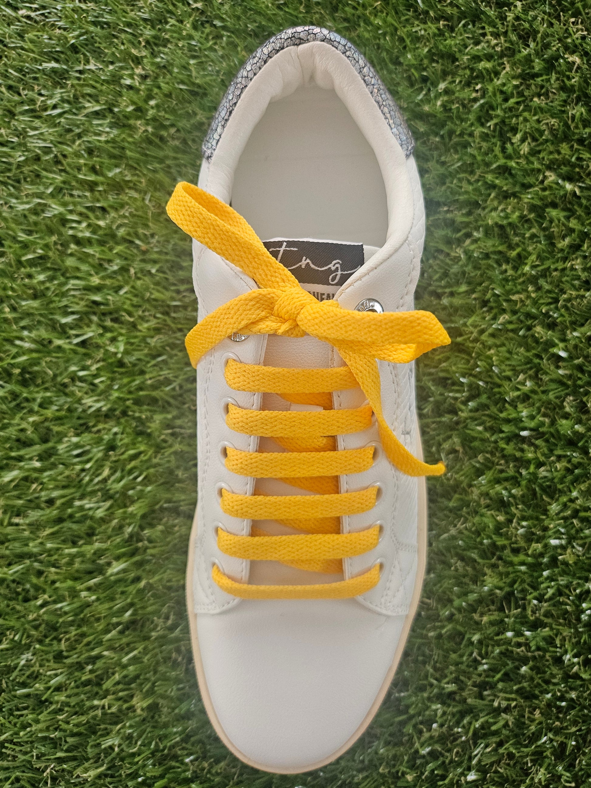 White sneaker with yellow laces on a grass background