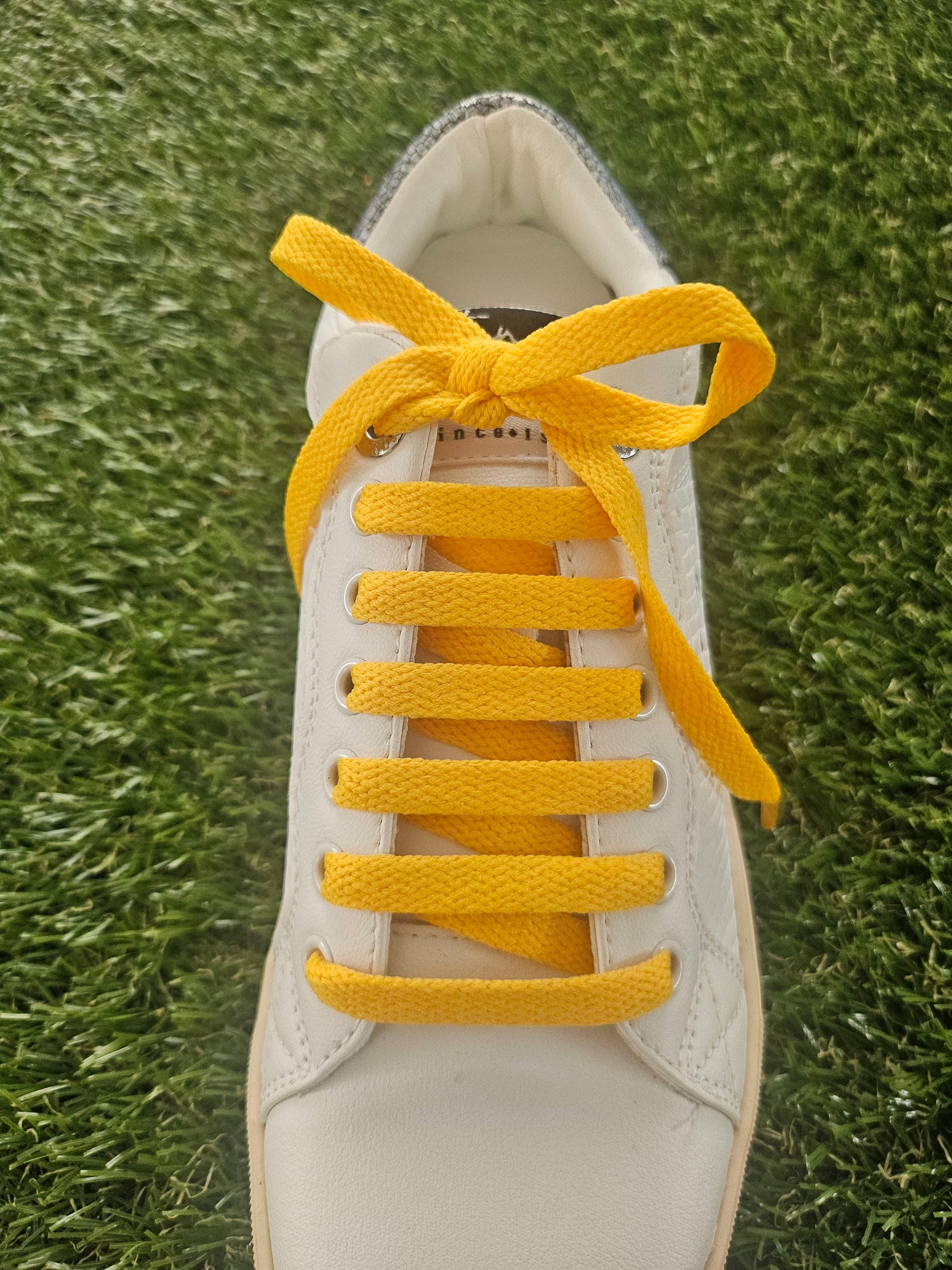 White sneaker with yellow laces on a grass background