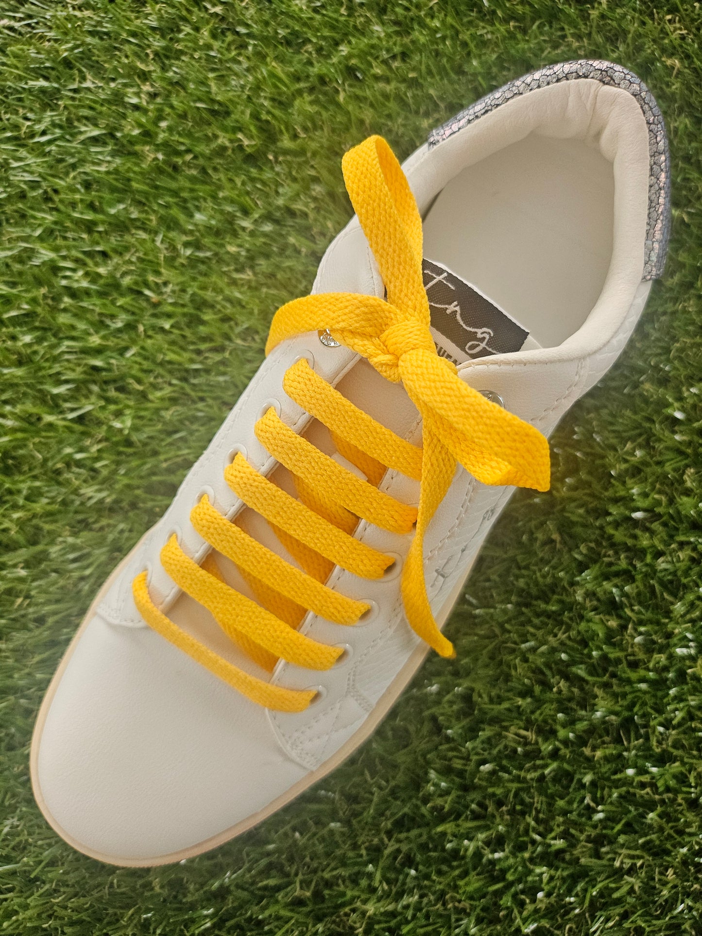 White sneaker with yellow laces on grass