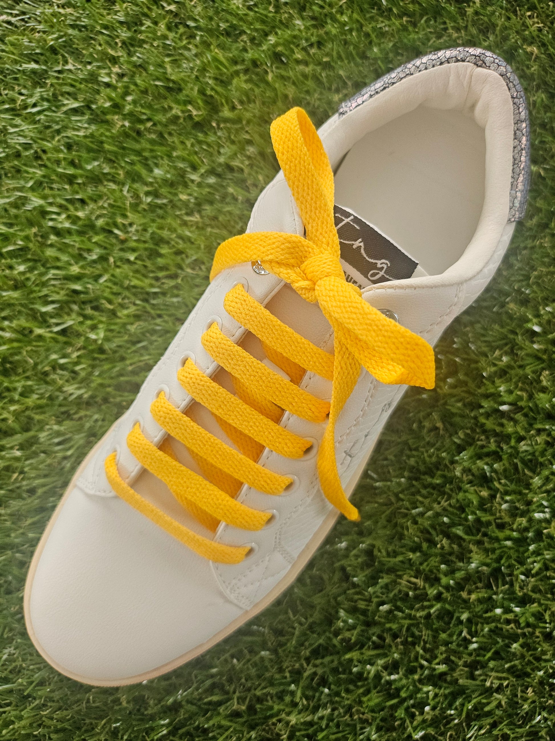 White sneaker with yellow laces on grass