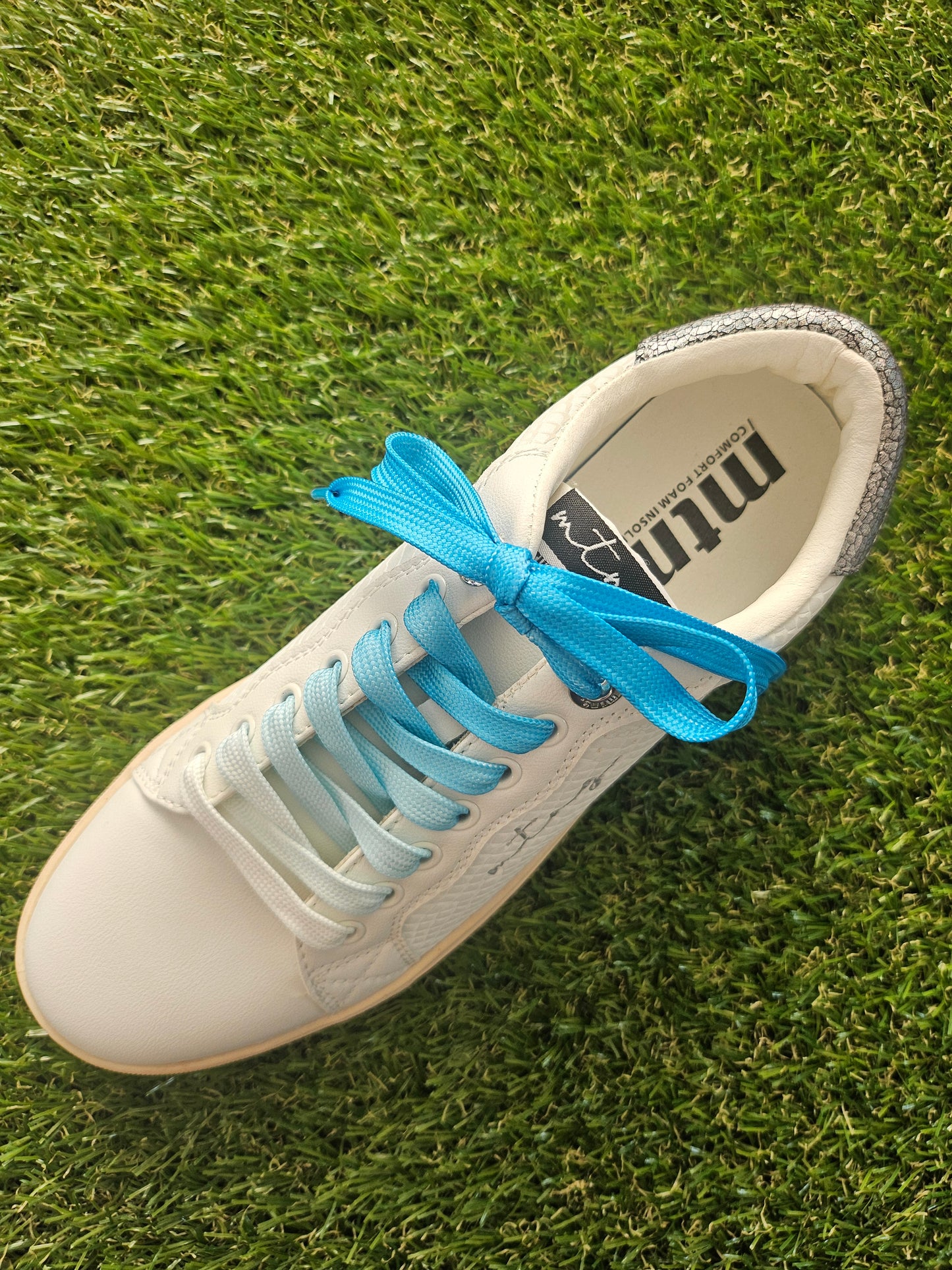White sneaker with blue laces on grass