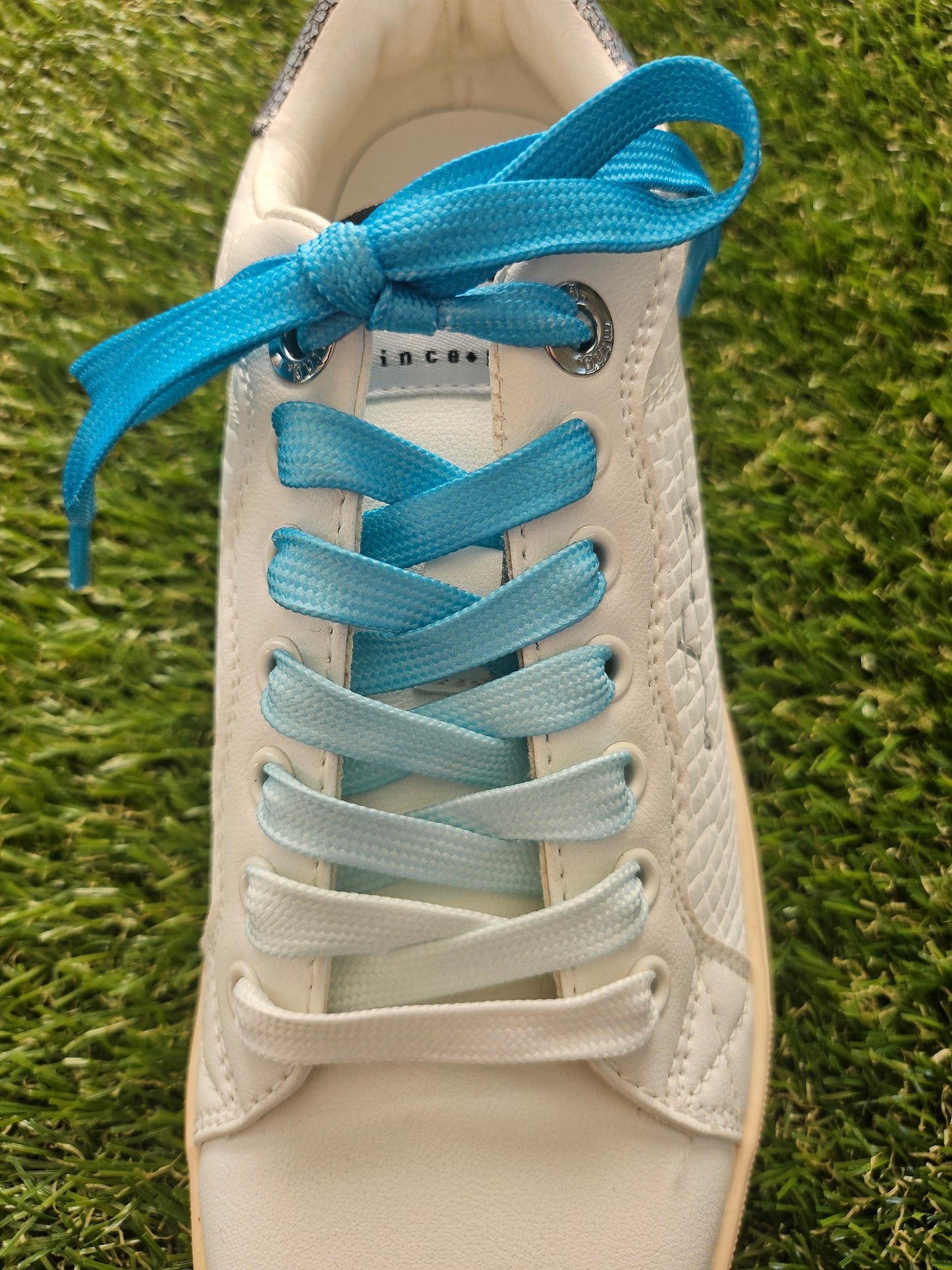 White sneaker with blue and light gray shoelaces on grass