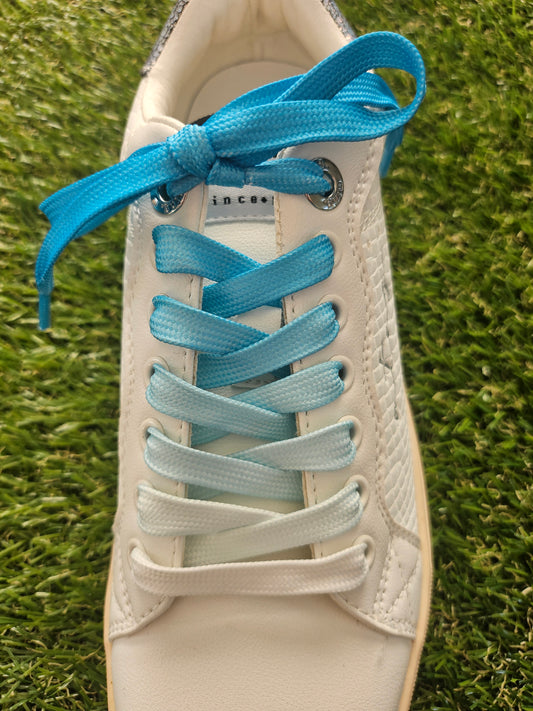 White sneaker with blue and light gray shoelaces on grass