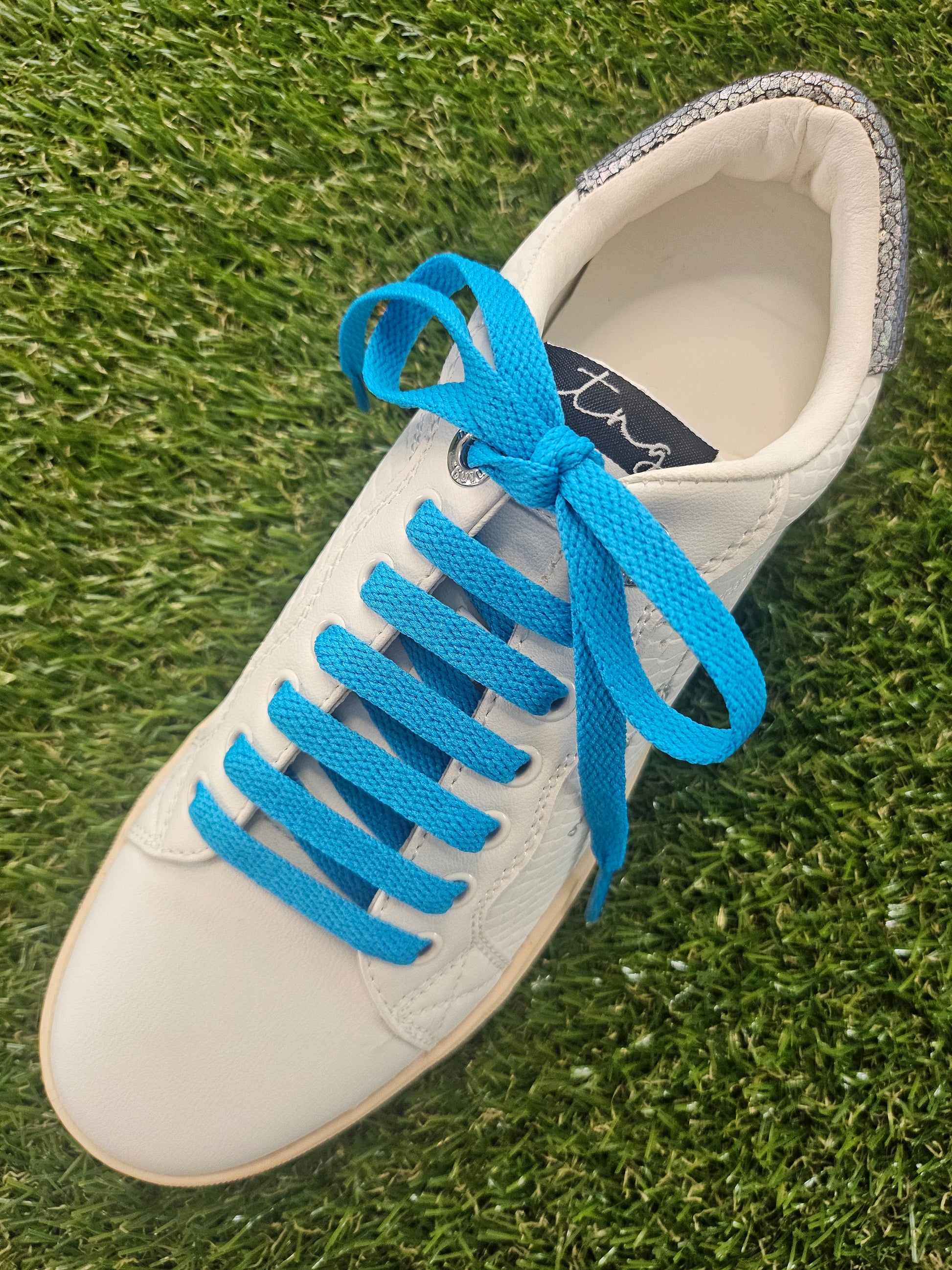 White sneaker with blue laces on a grass background