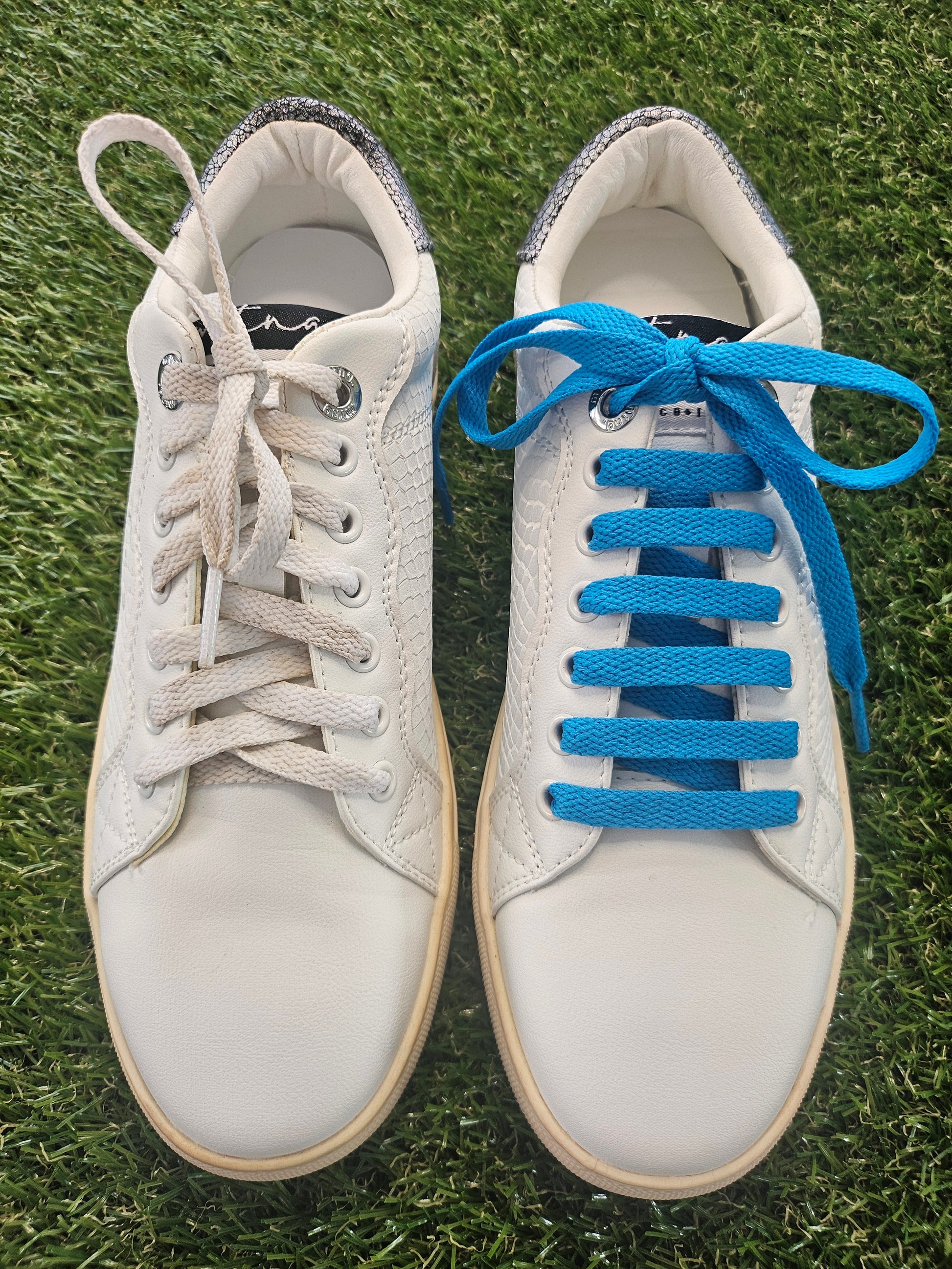 White sneakers with blue and beige laces on grass