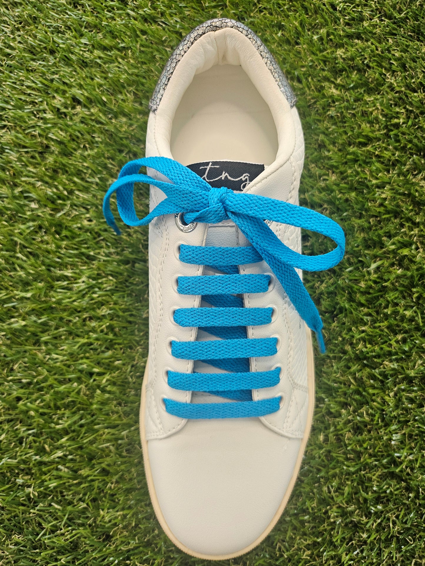 White sneaker with blue laces on a grass background