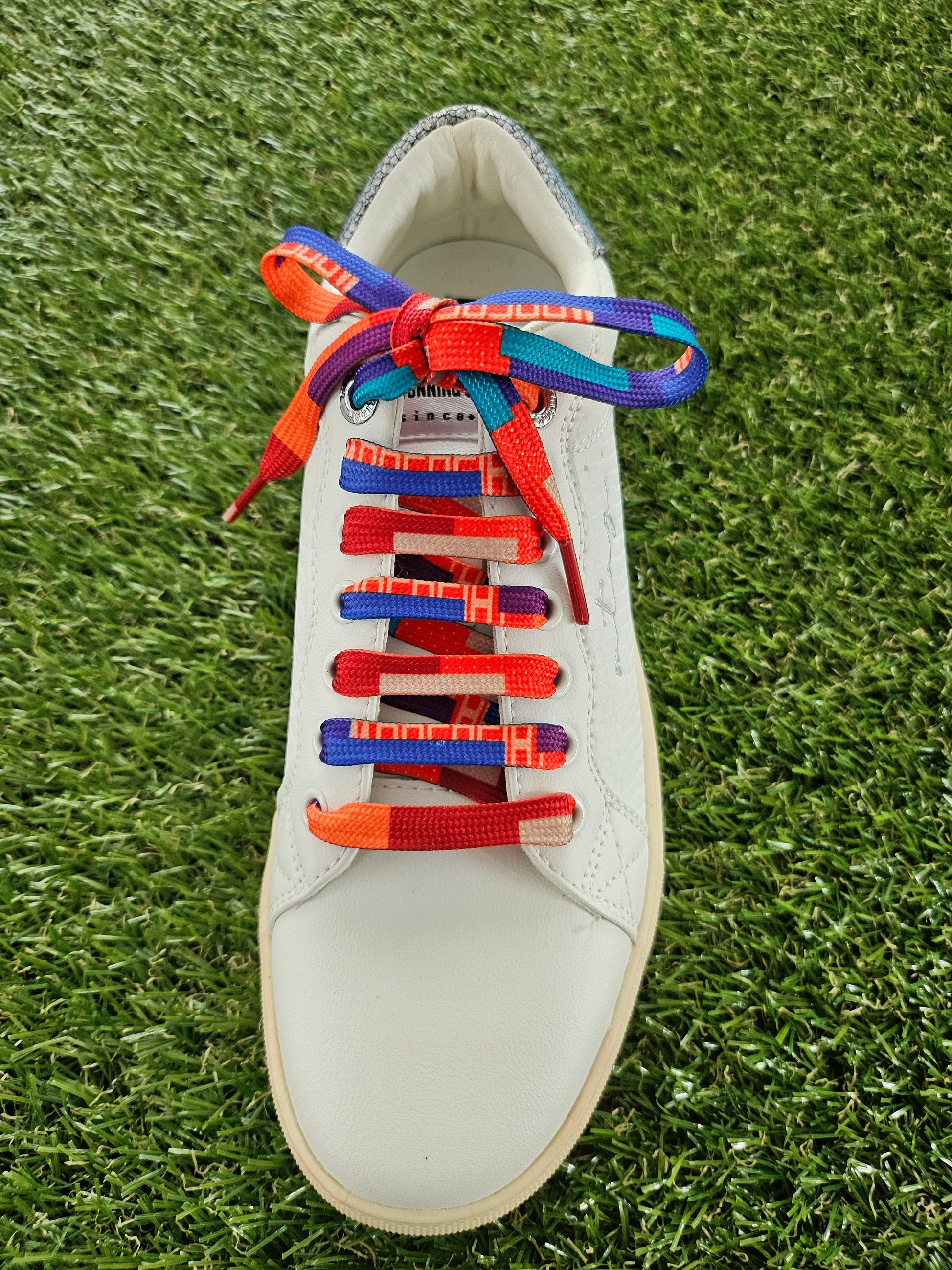 White sneaker with colourful patterned laces on a grass background