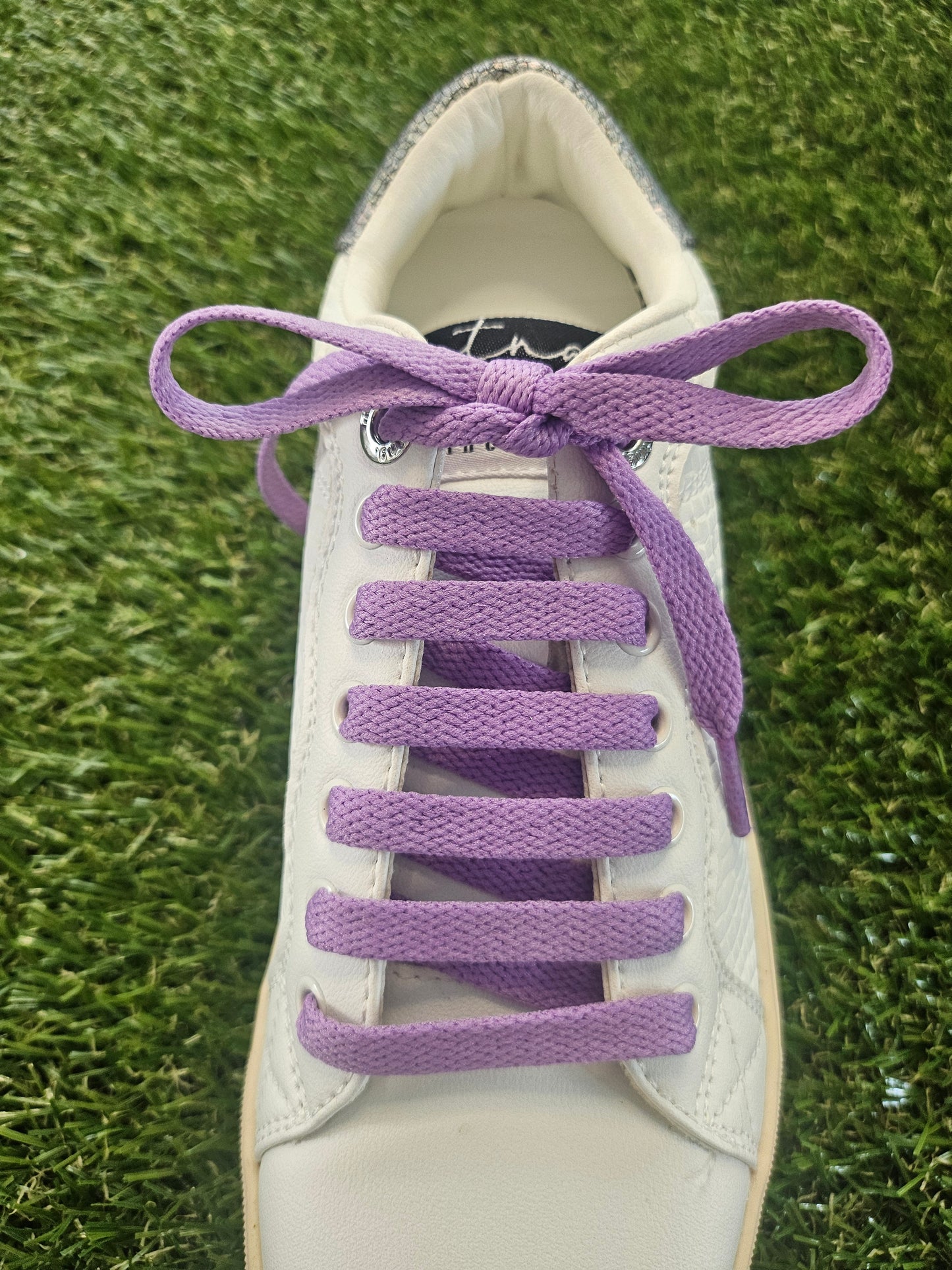 White sneaker with purple shoelaces on a grass background