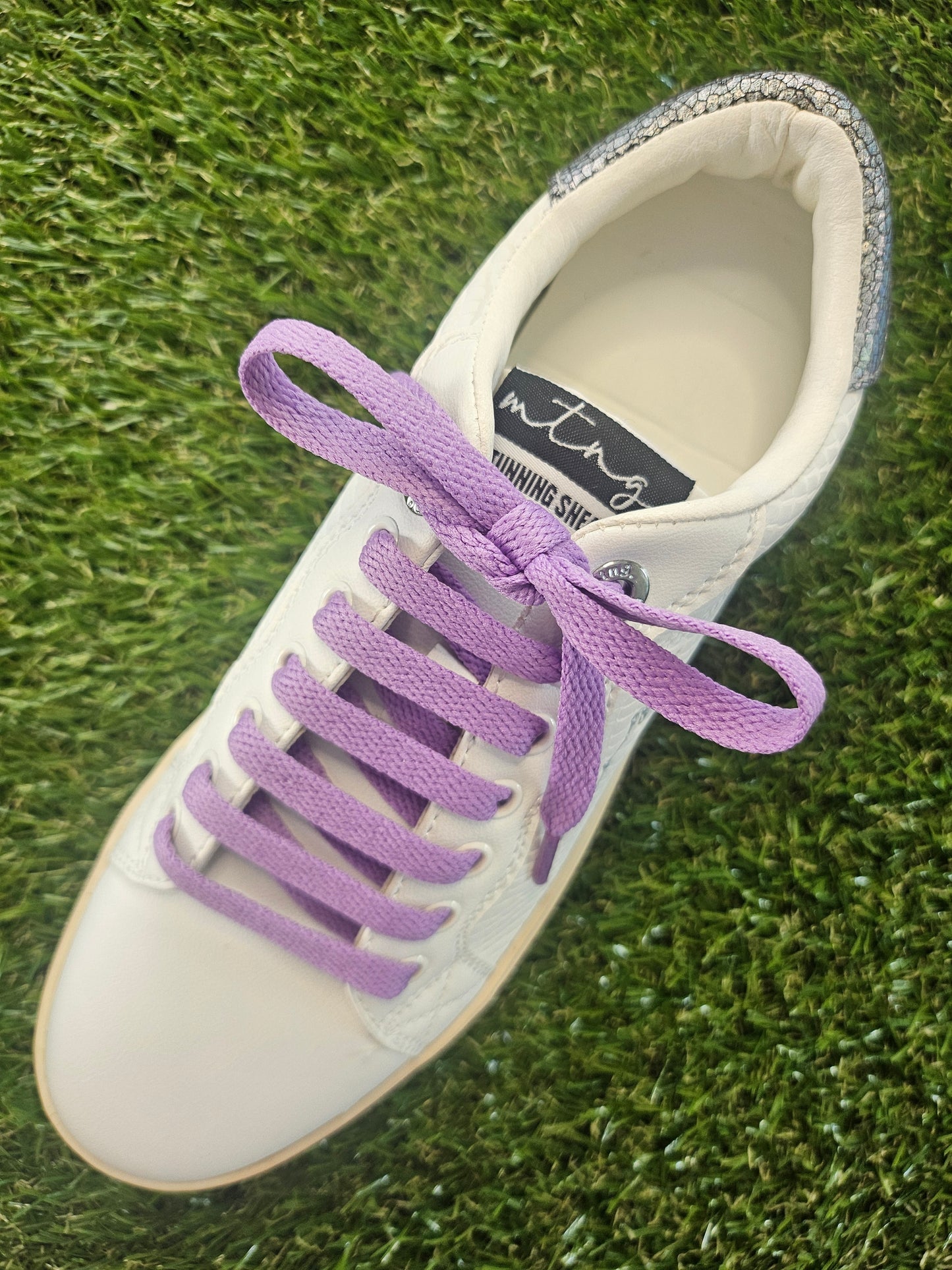 White sneaker with purple laces on a grass background