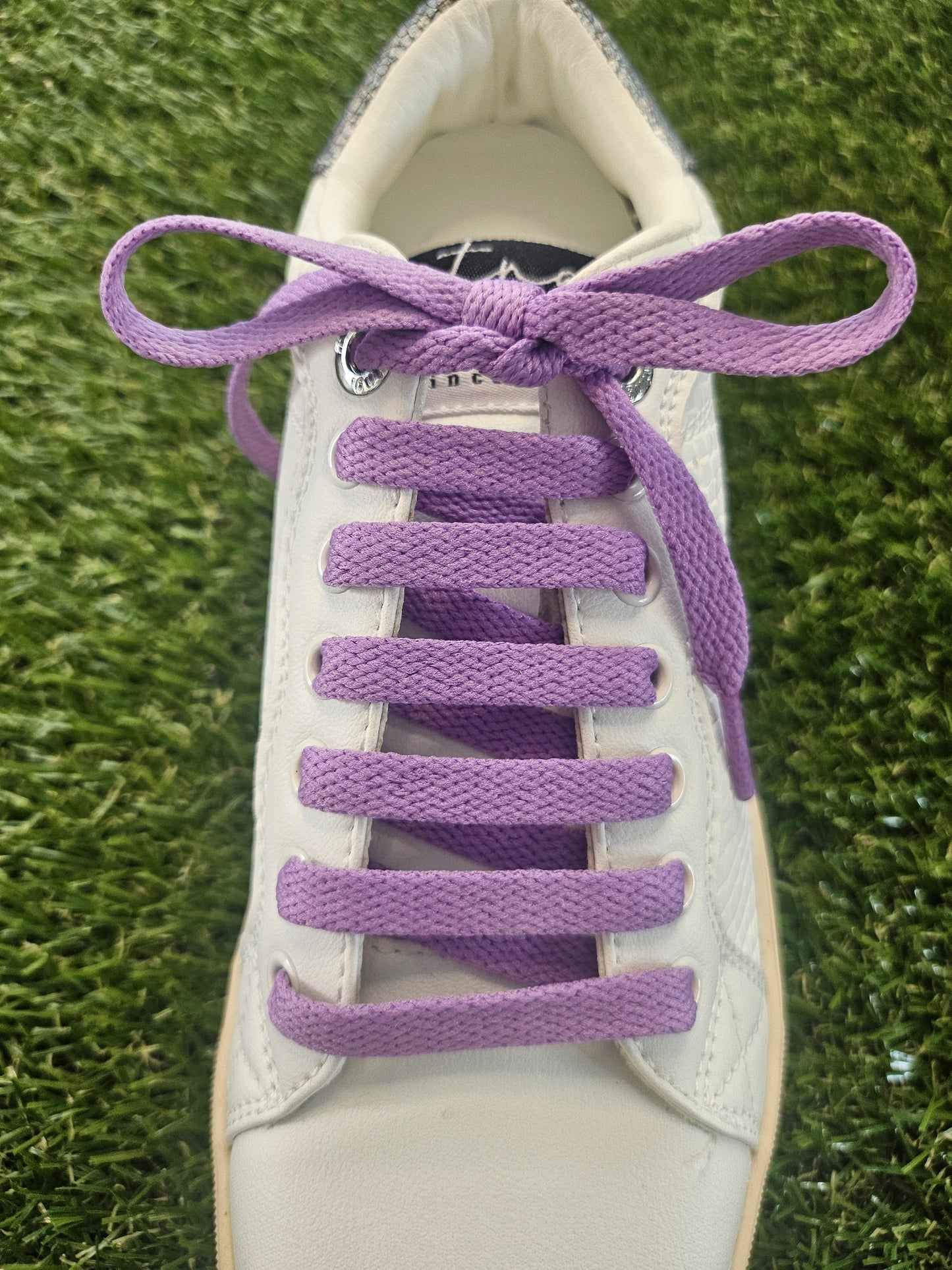White sneaker with purple shoelaces on a grass background