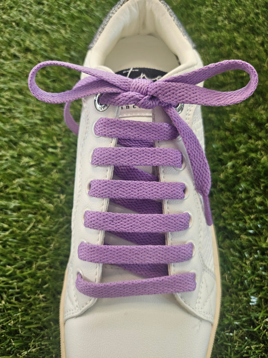 White sneaker with purple shoelaces on a grass background